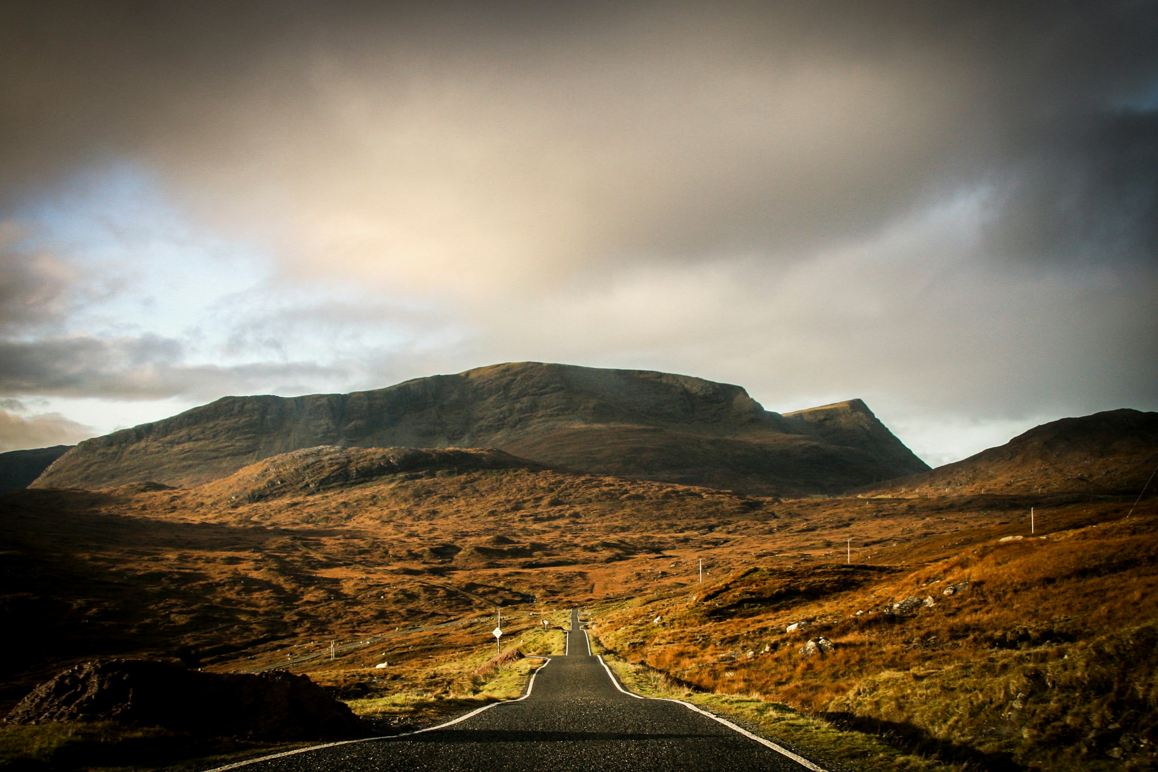 An empty road running through moorland hills in low golden light