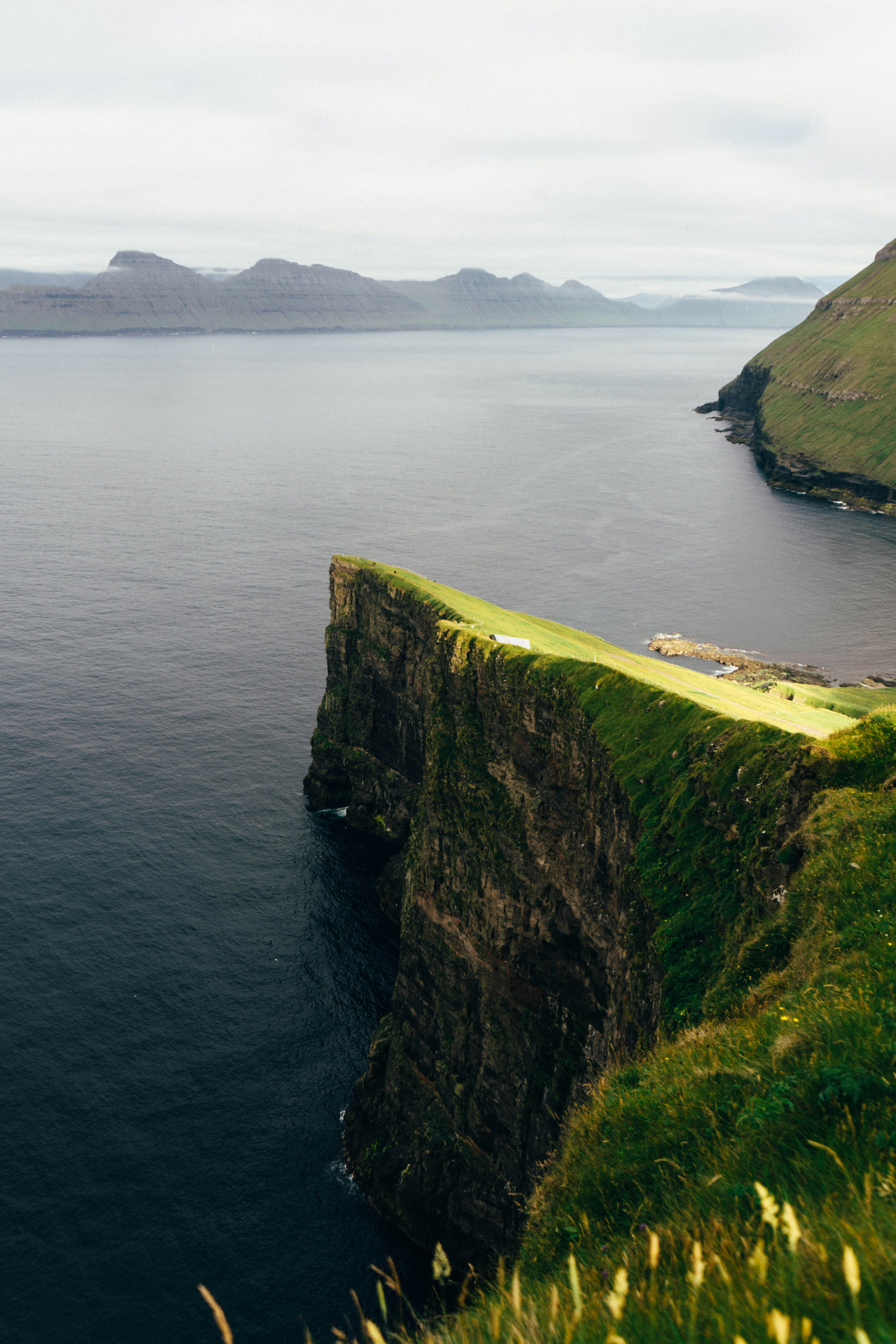 A grass-topped sea cliff dropping to dark water with islands on the horizon