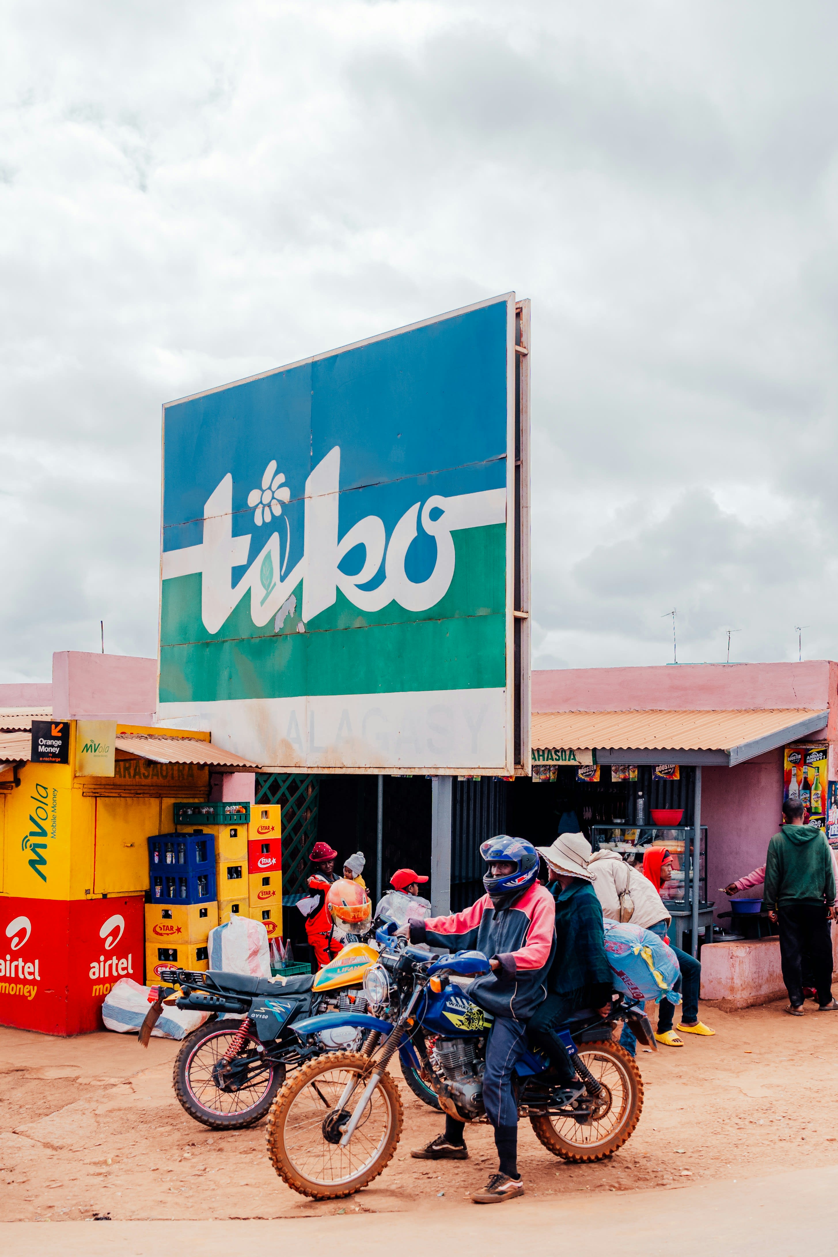 Motorbikes passing shopfronts below a large faded blue sign