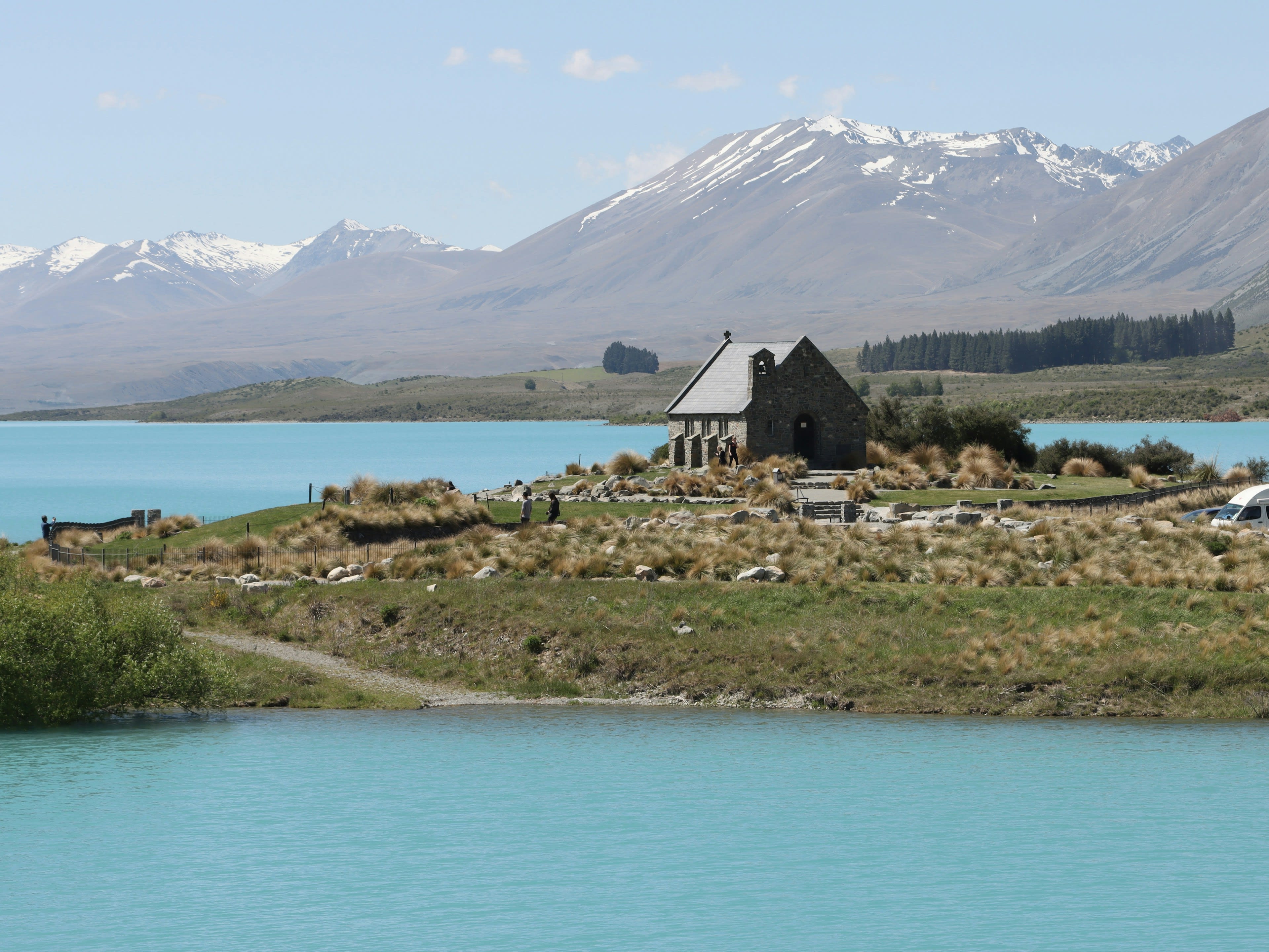 A small stone church beside a milky turquoise lake with mountains behind