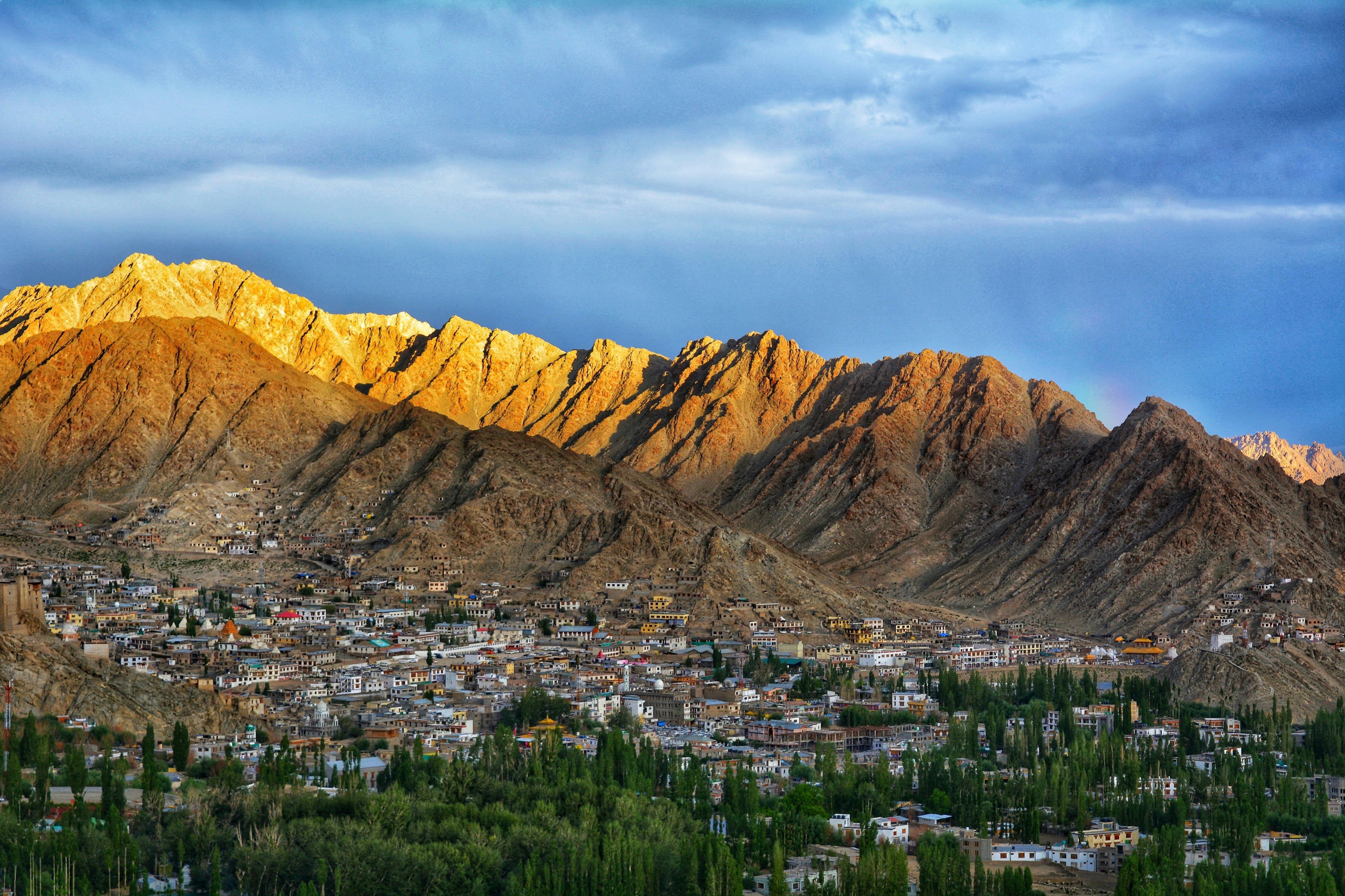 A town of white buildings in a green valley with a bare golden range catching low sun above it