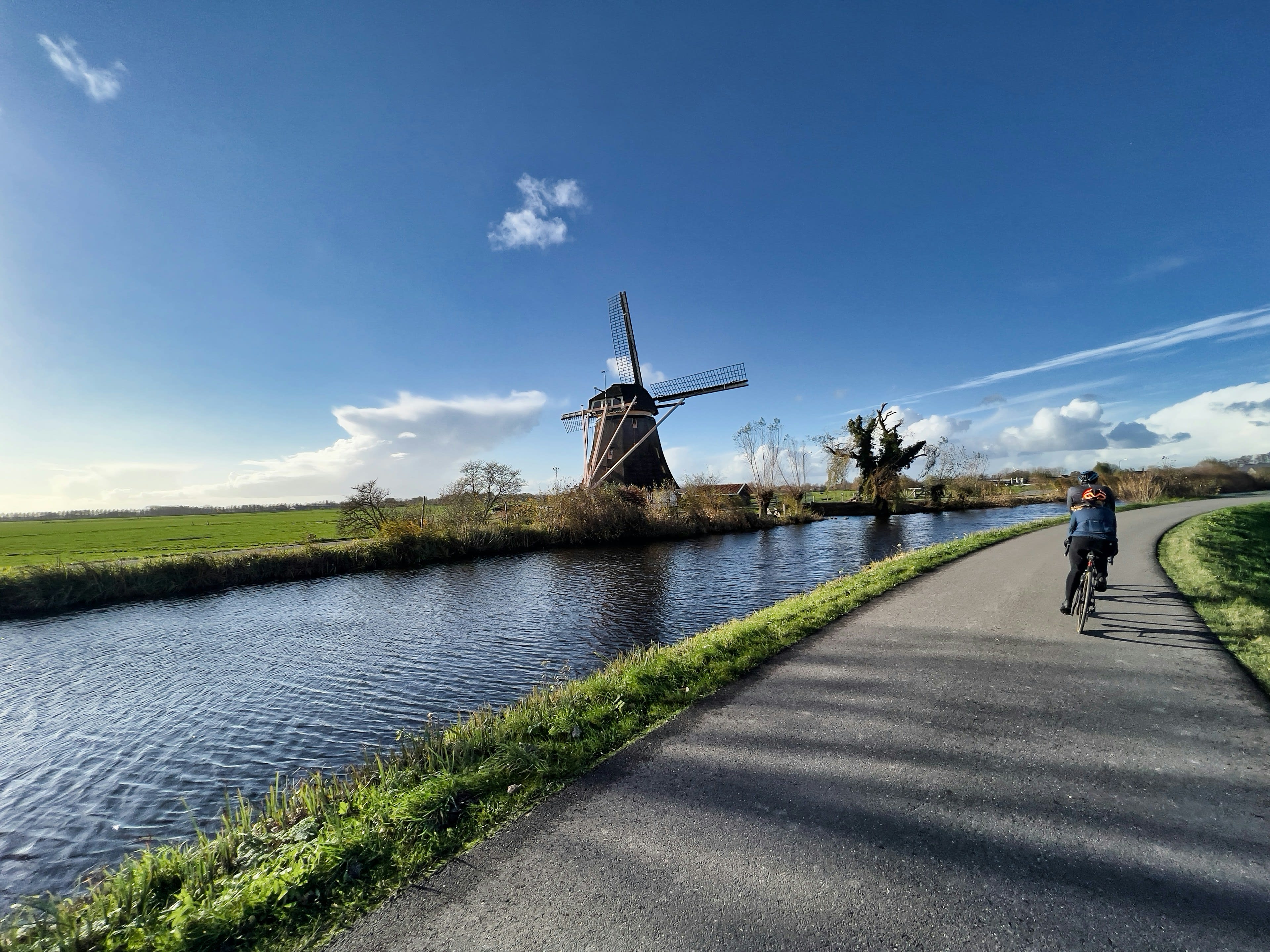 A cyclist on a dike path passing a historic windmill by the water