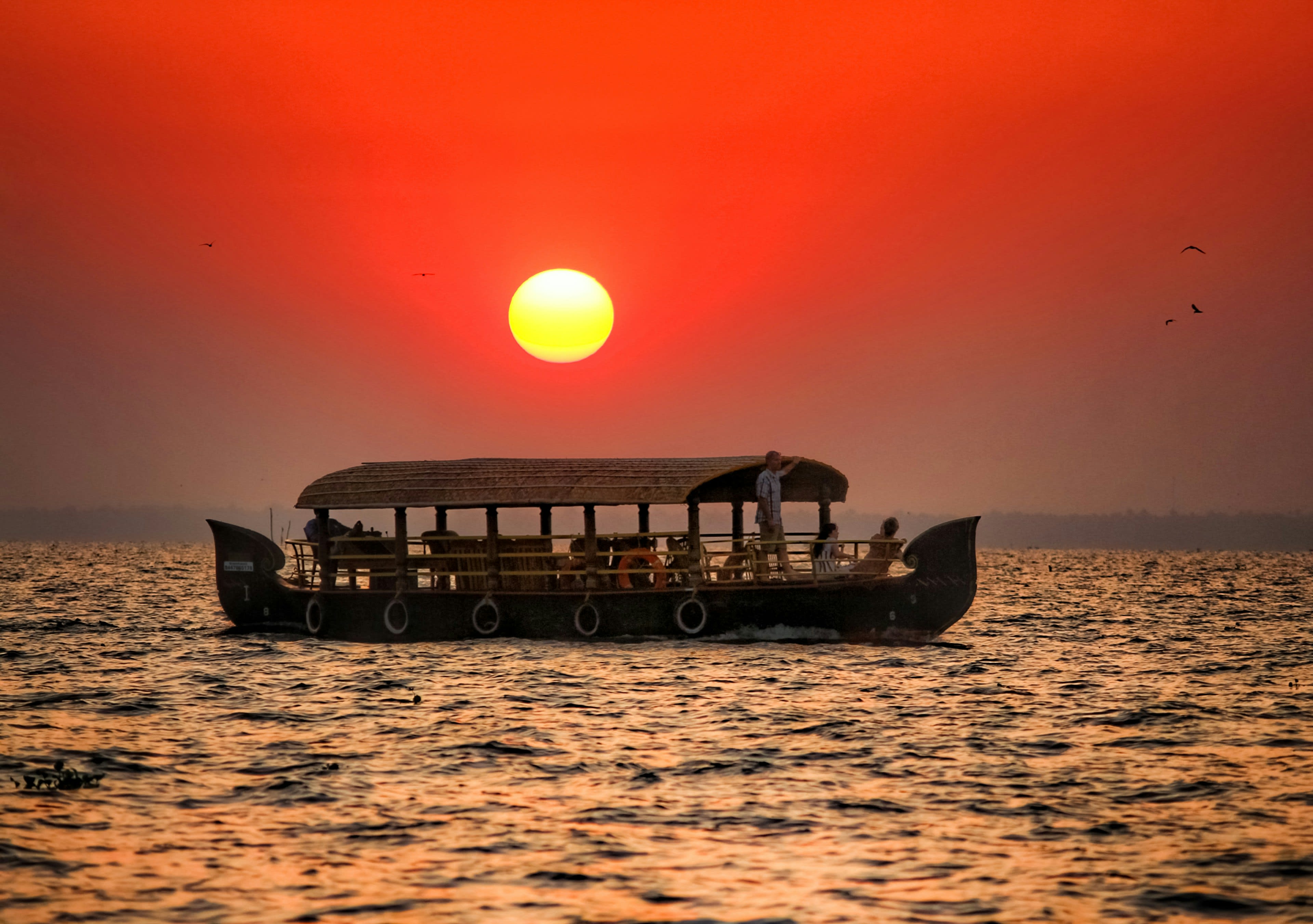 A houseboat silhouetted on still water beneath a large red setting sun