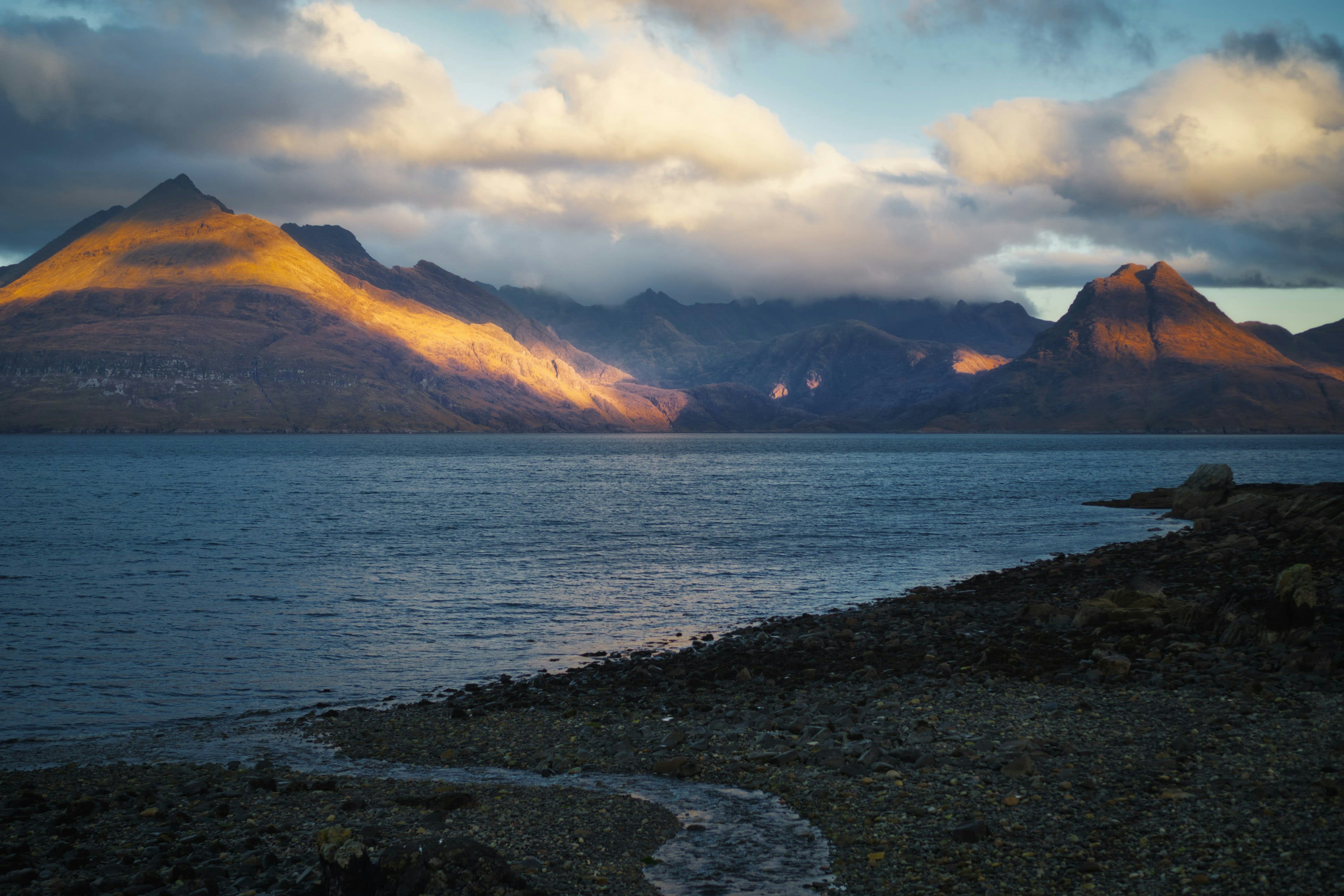 A dark serrated mountain ridge lit orange across a calm sea loch