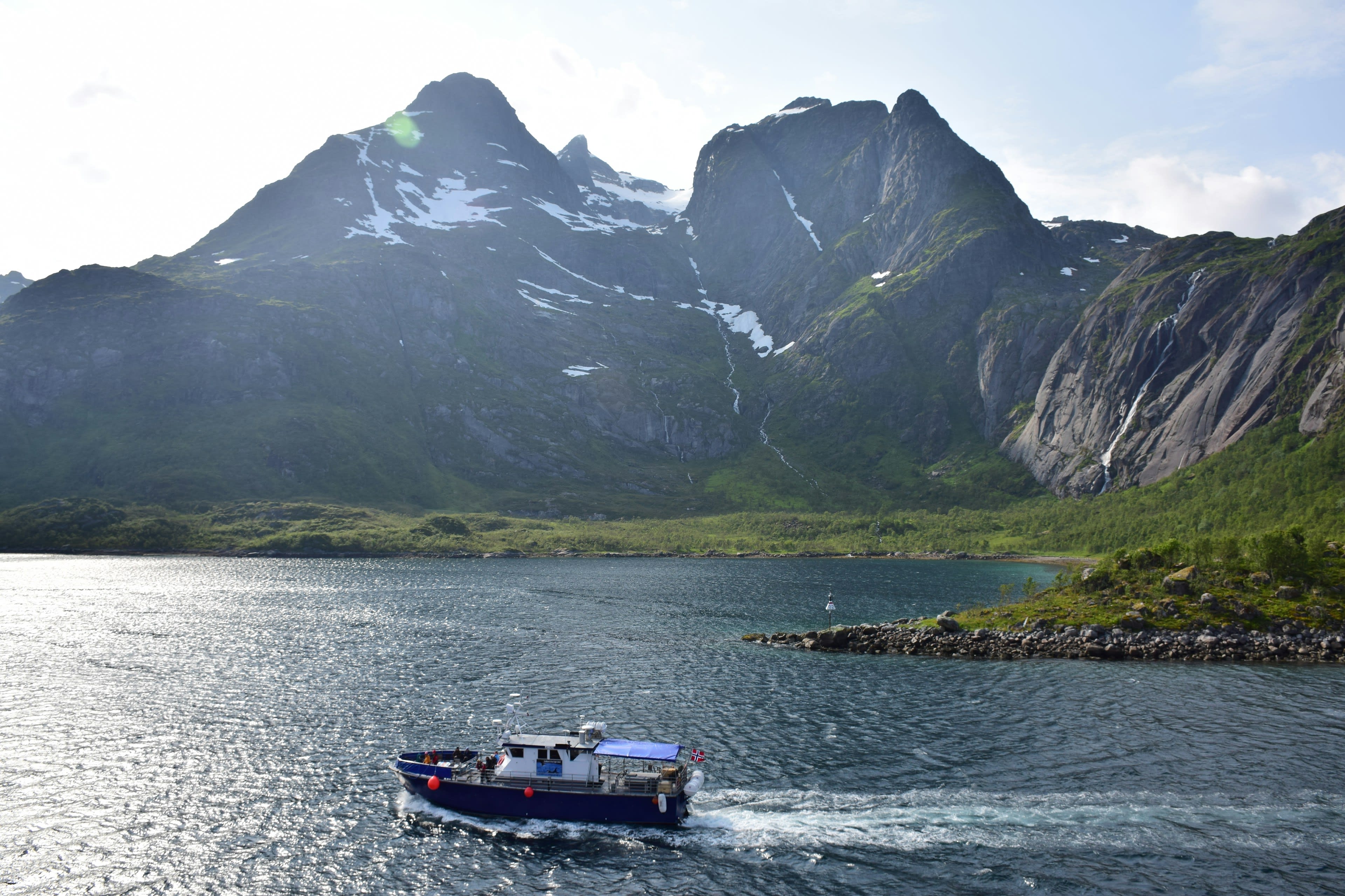 A small boat on grey water below a steep snow-streaked mountain