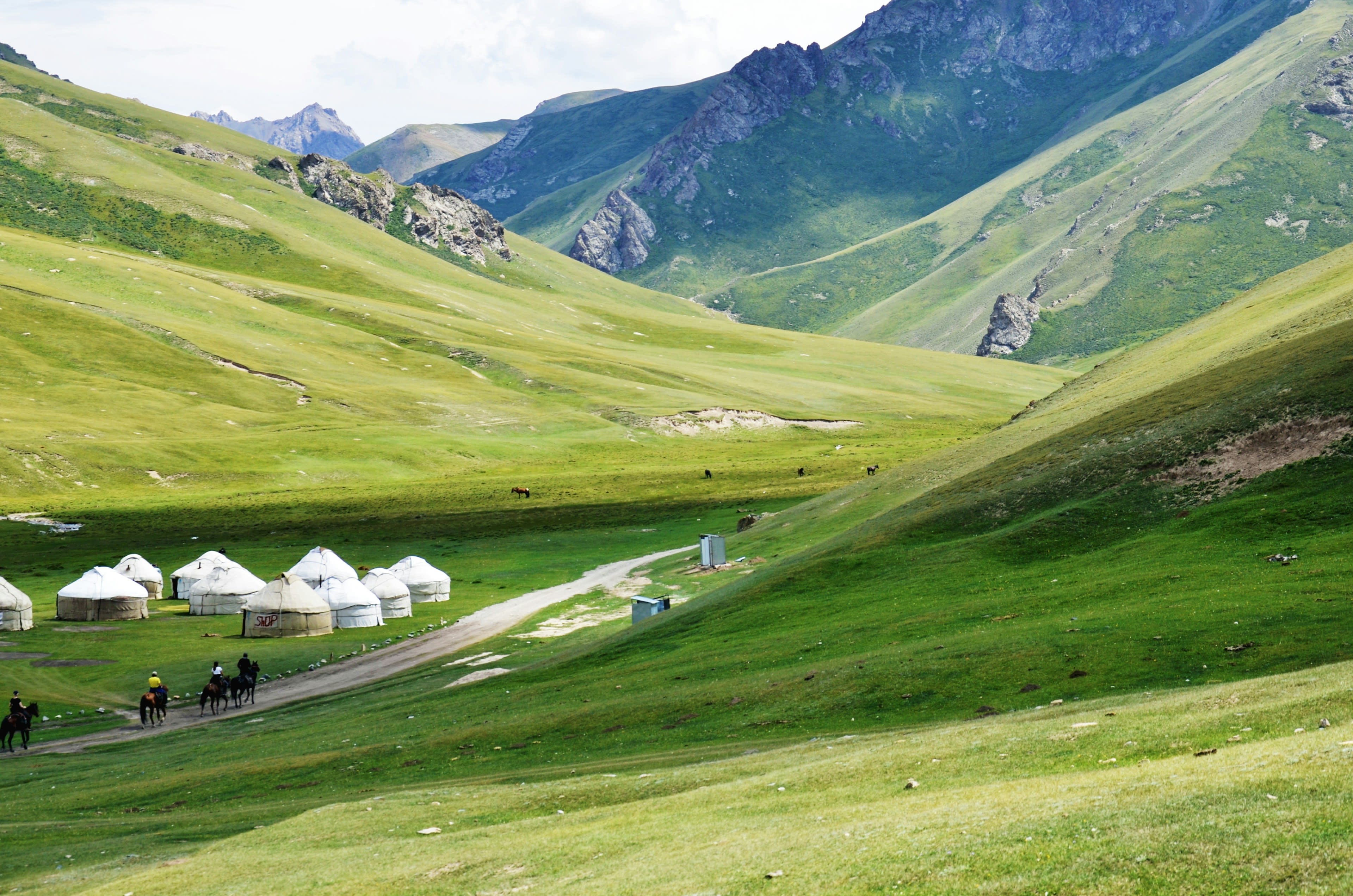 White yurts scattered across a wide green valley below rounded mountains
