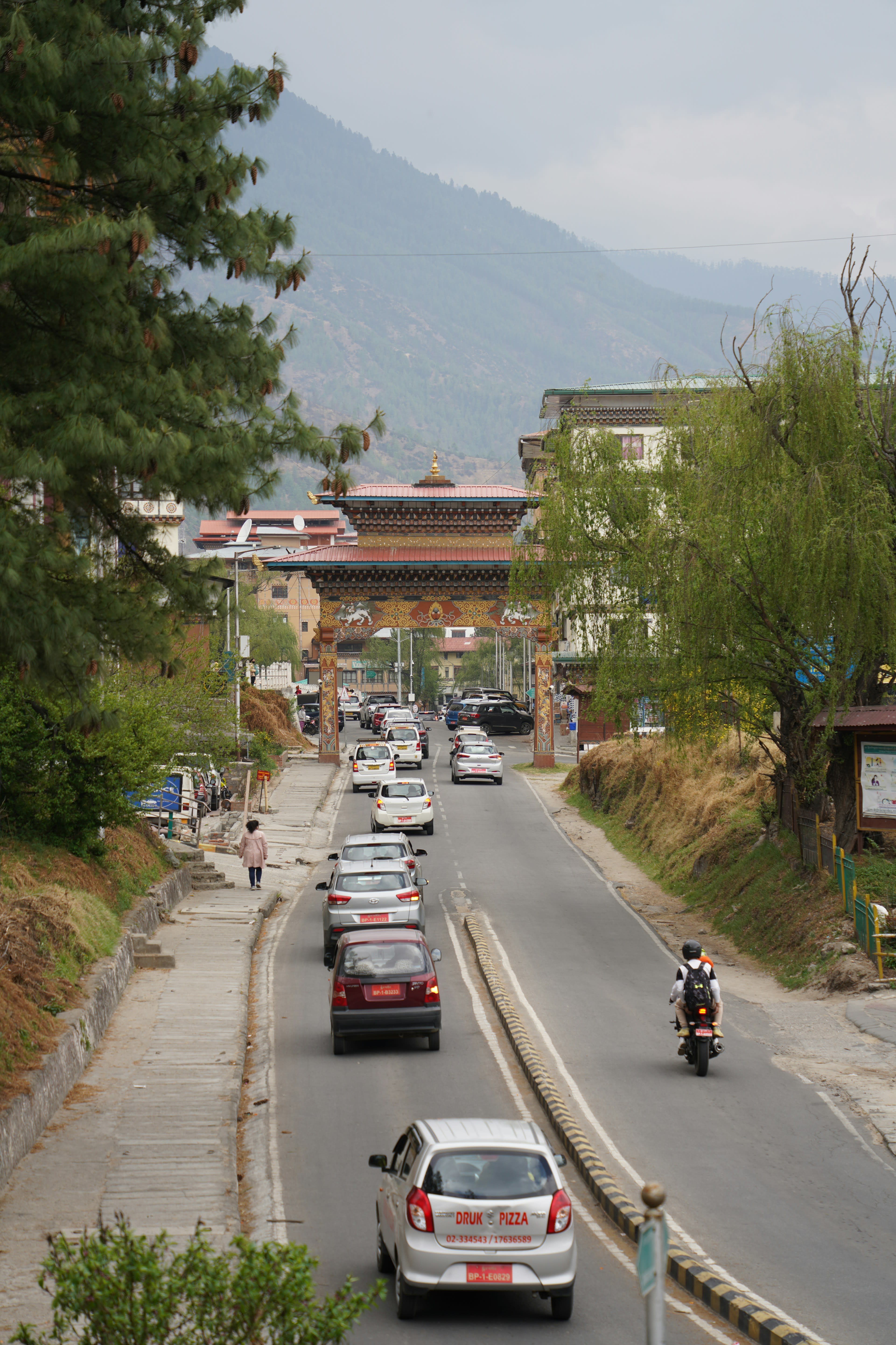 A busy town road running downhill between buildings with forested mountains beyond
