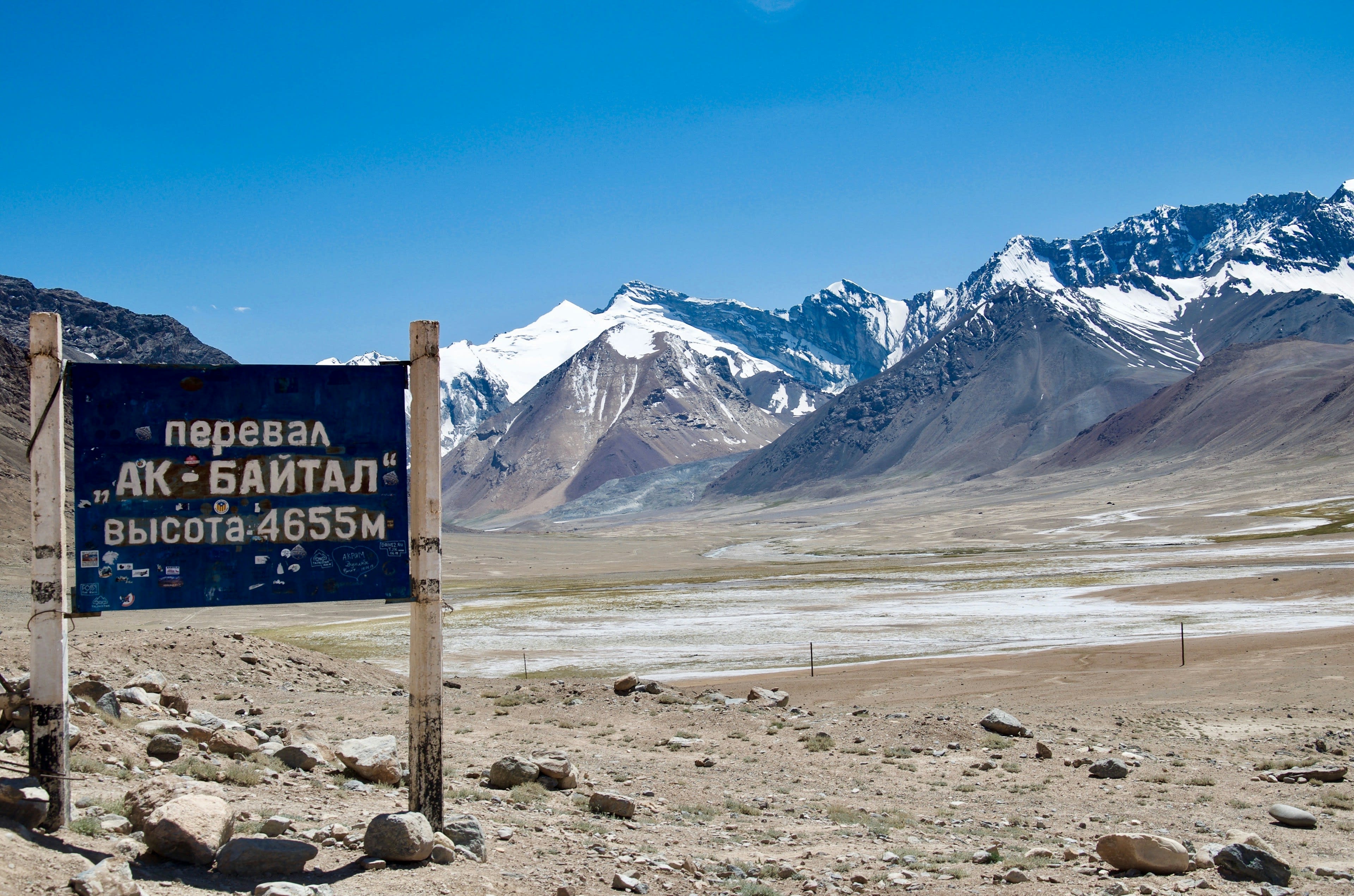 The Ak-Baital pass sign with snow-dusted peaks behind