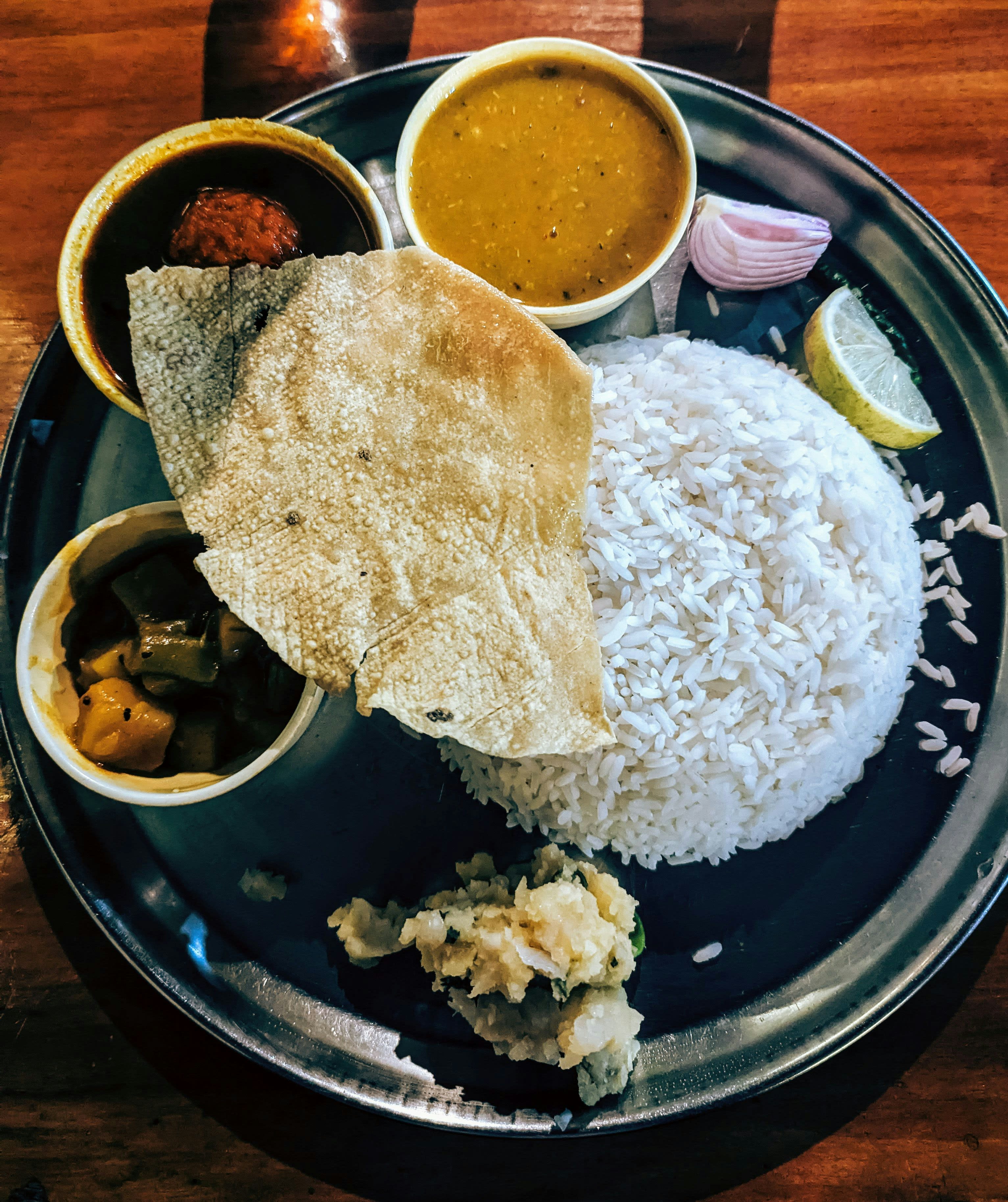 A steel plate of rice, curries and fried fish on a table
