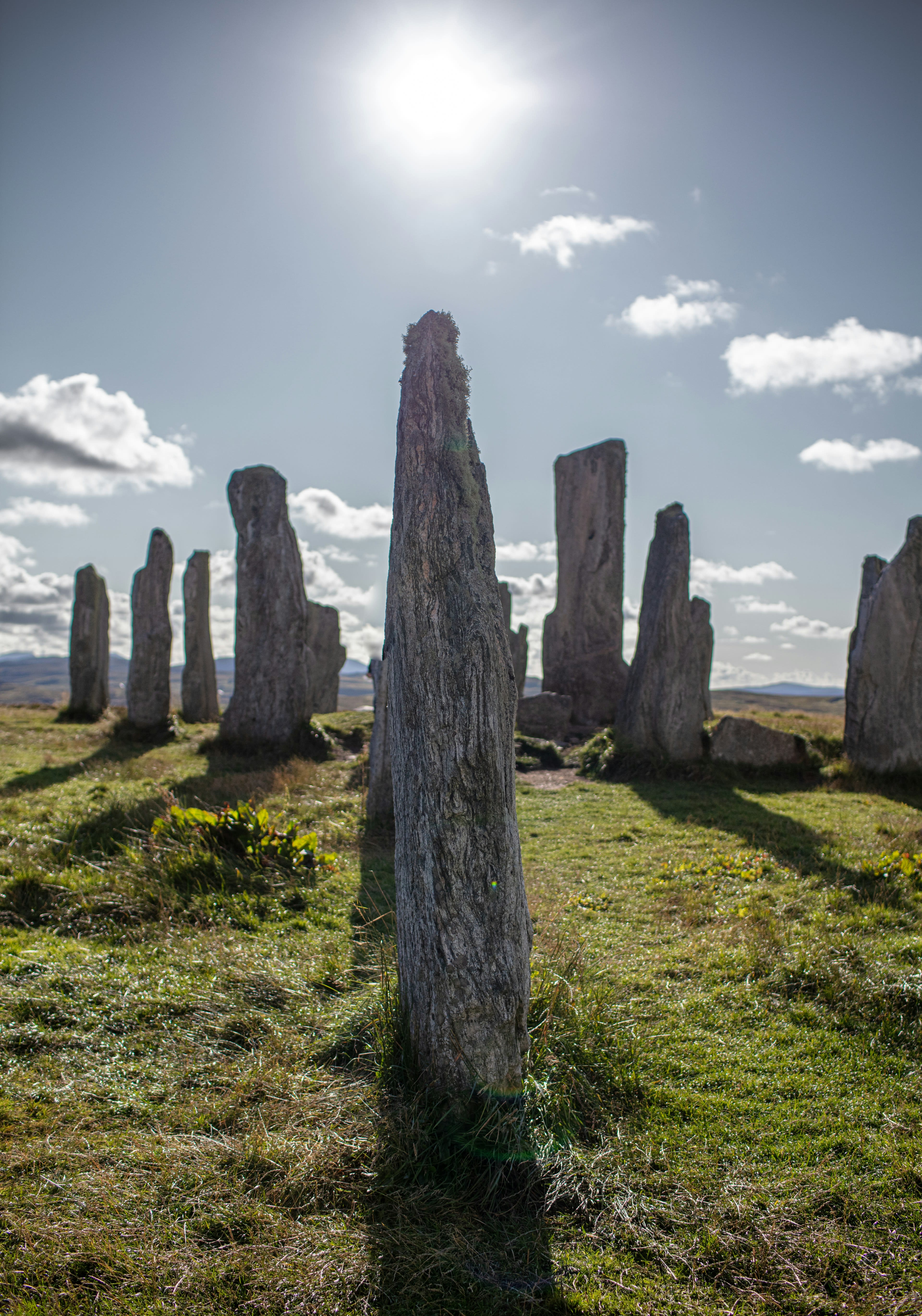 Tall standing stones on green grass under a bright sky with sun flare