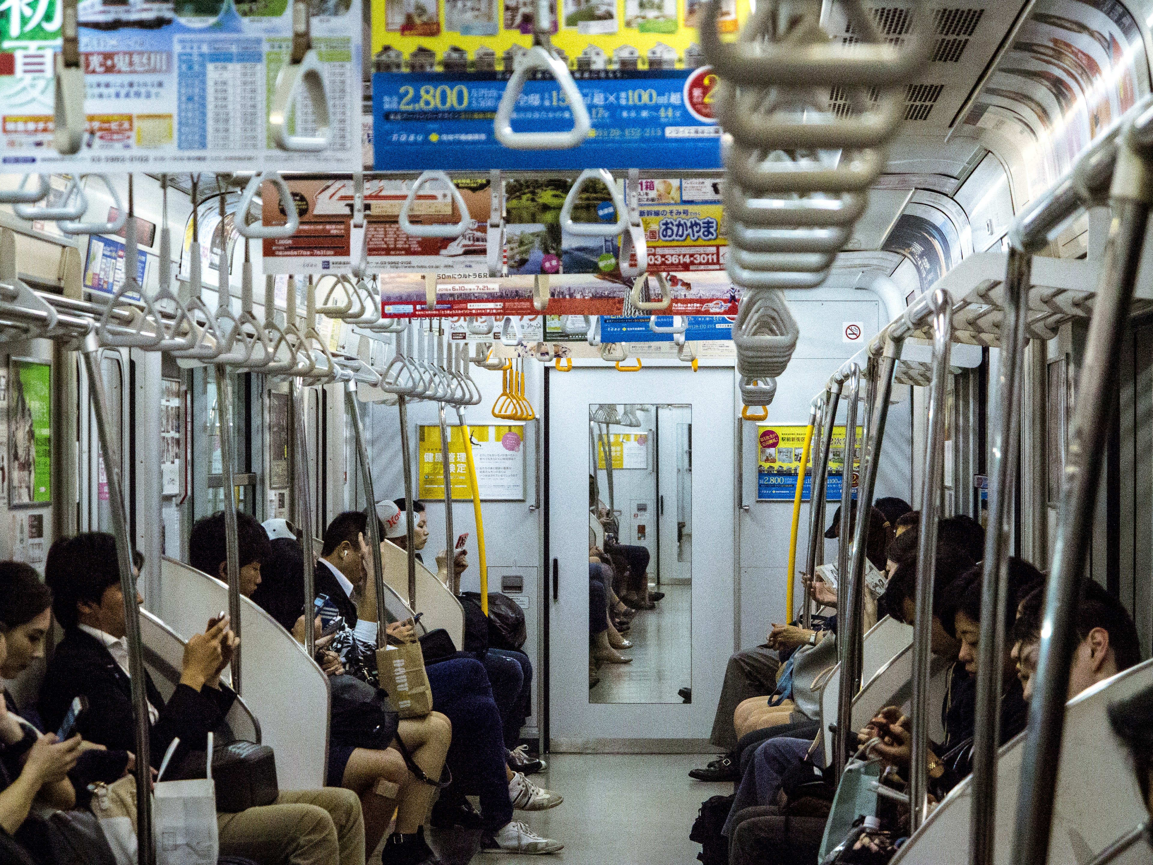 Passengers seated along a subway carriage with hanging straps and Japanese advertising