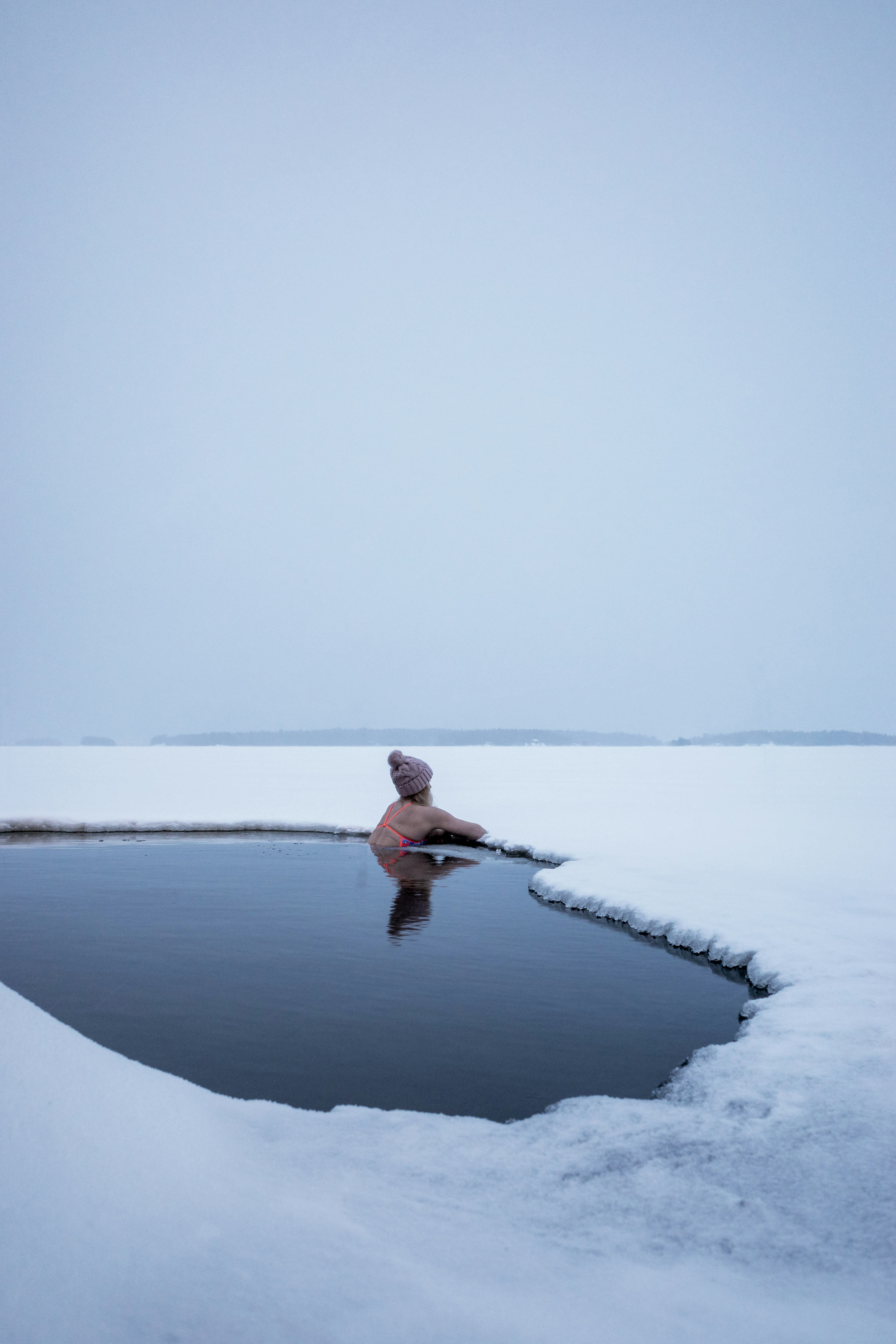 A person bathing in a hole cut in lake ice surrounded by snow