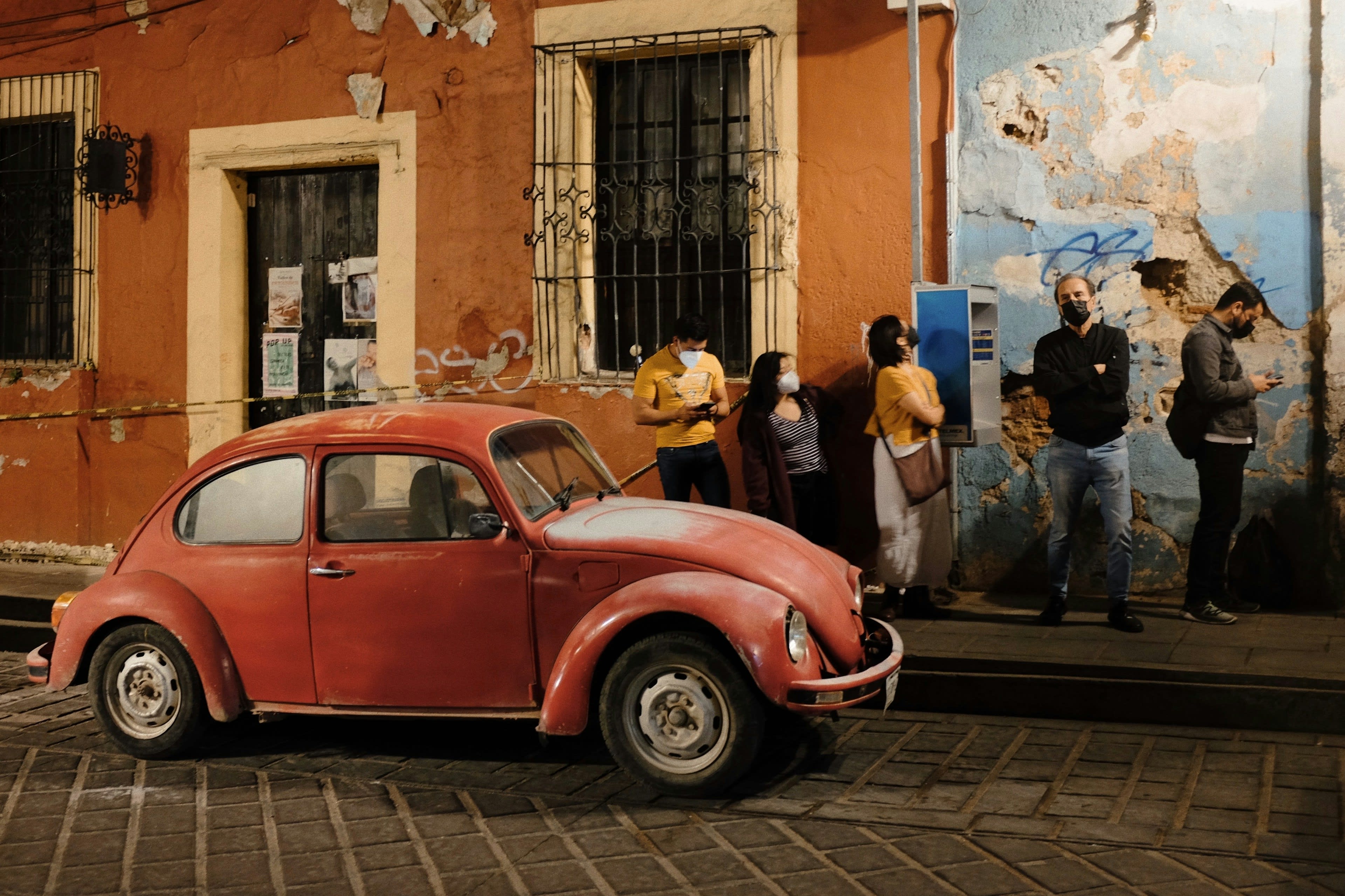 A red Volkswagen Beetle parked on cobbles in front of a painted wall