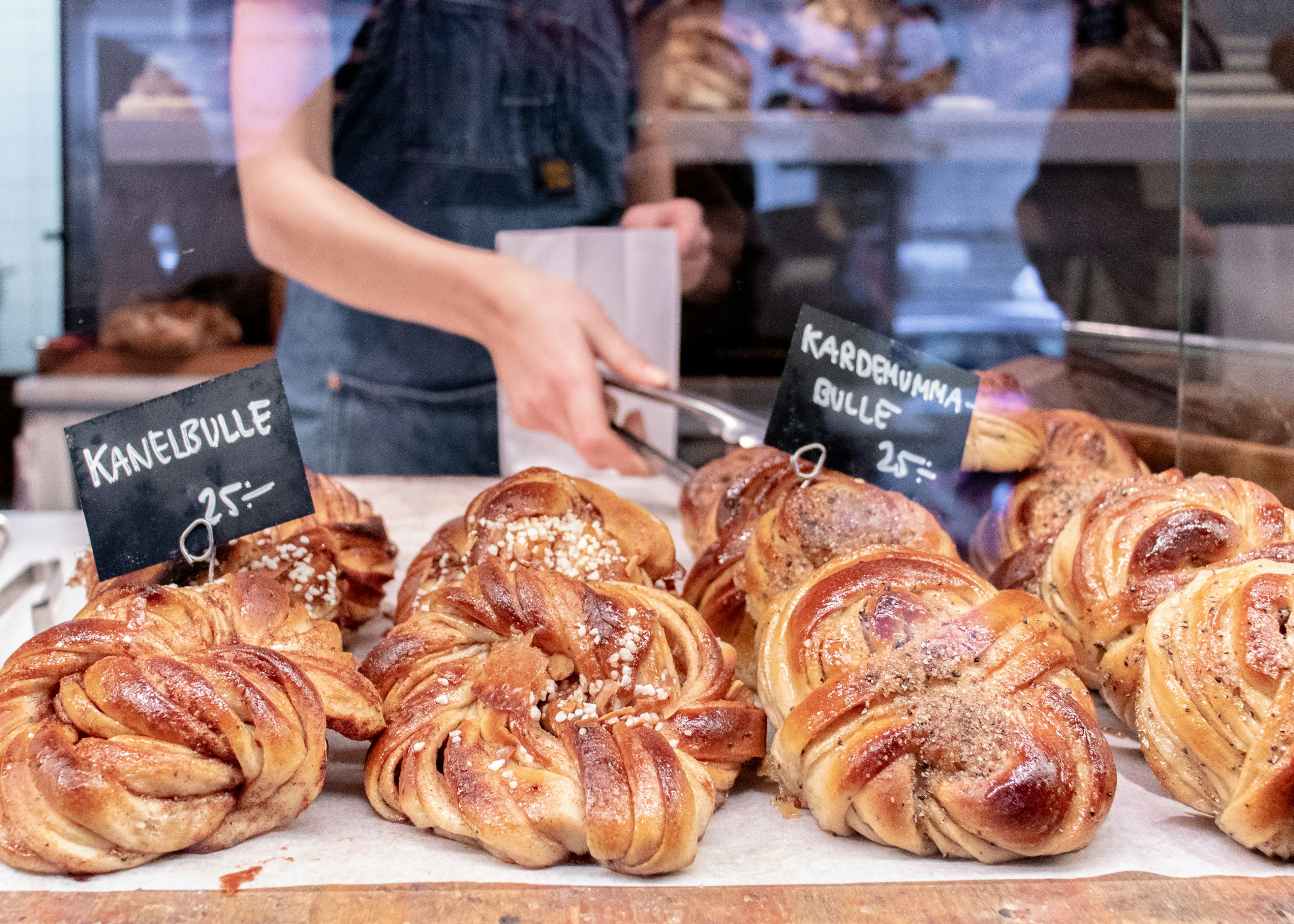 Trays of large cinnamon and cardamom buns in a bakery display with handwritten price signs