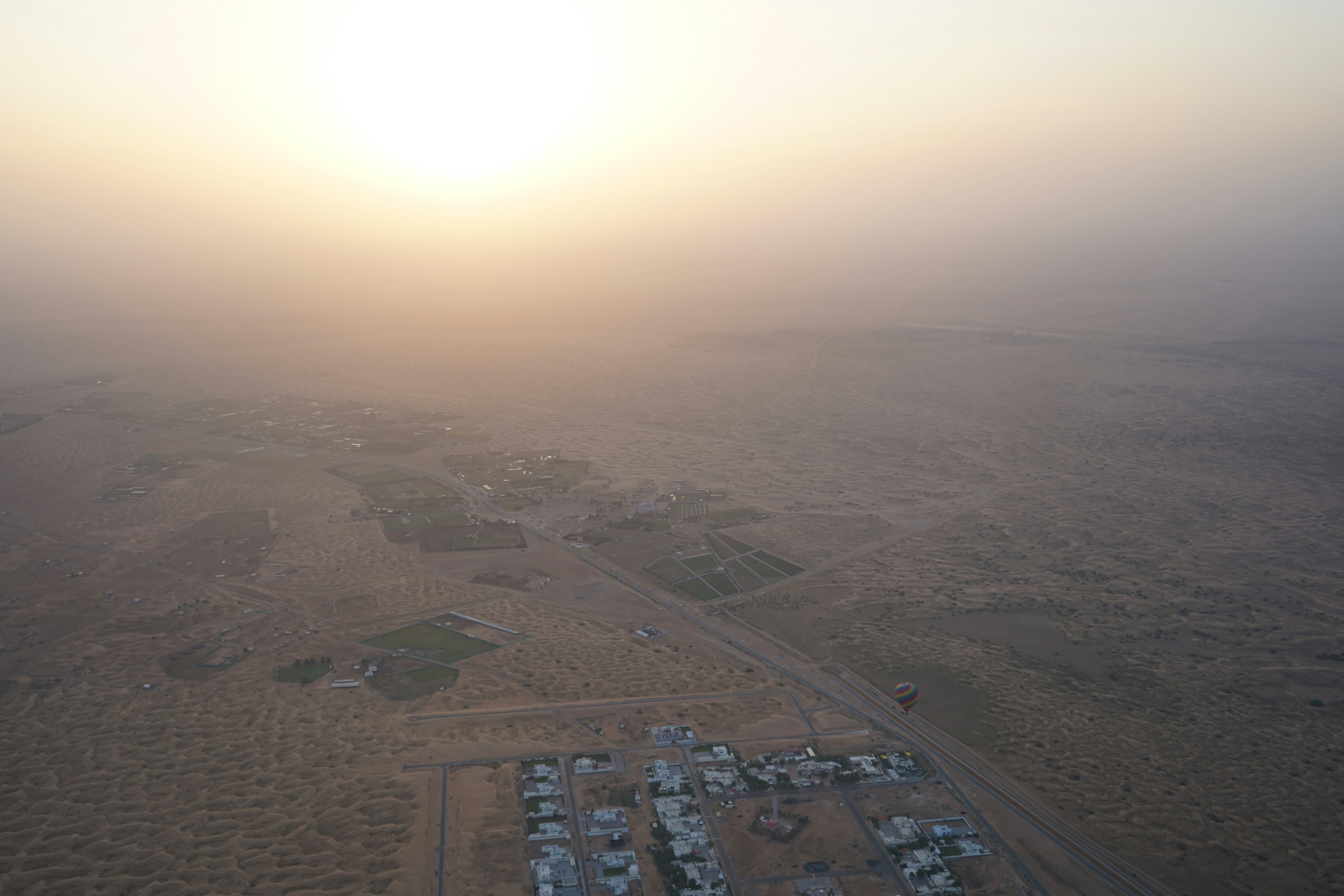 Aerial view of desert tent camps and tracks scattered across dunes in dawn haze