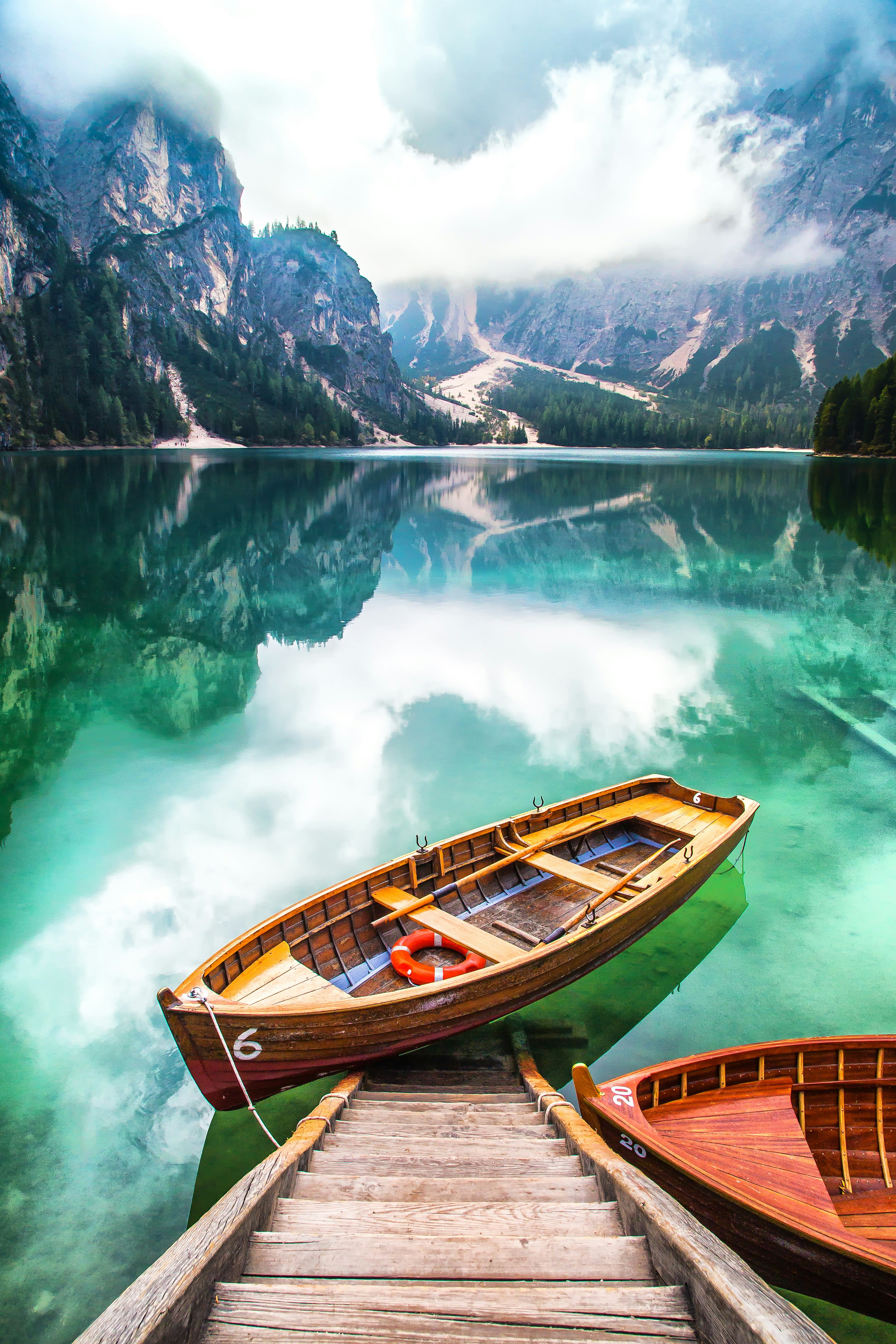 Wooden rowing boats moored on still green water beneath a rock wall at dawn