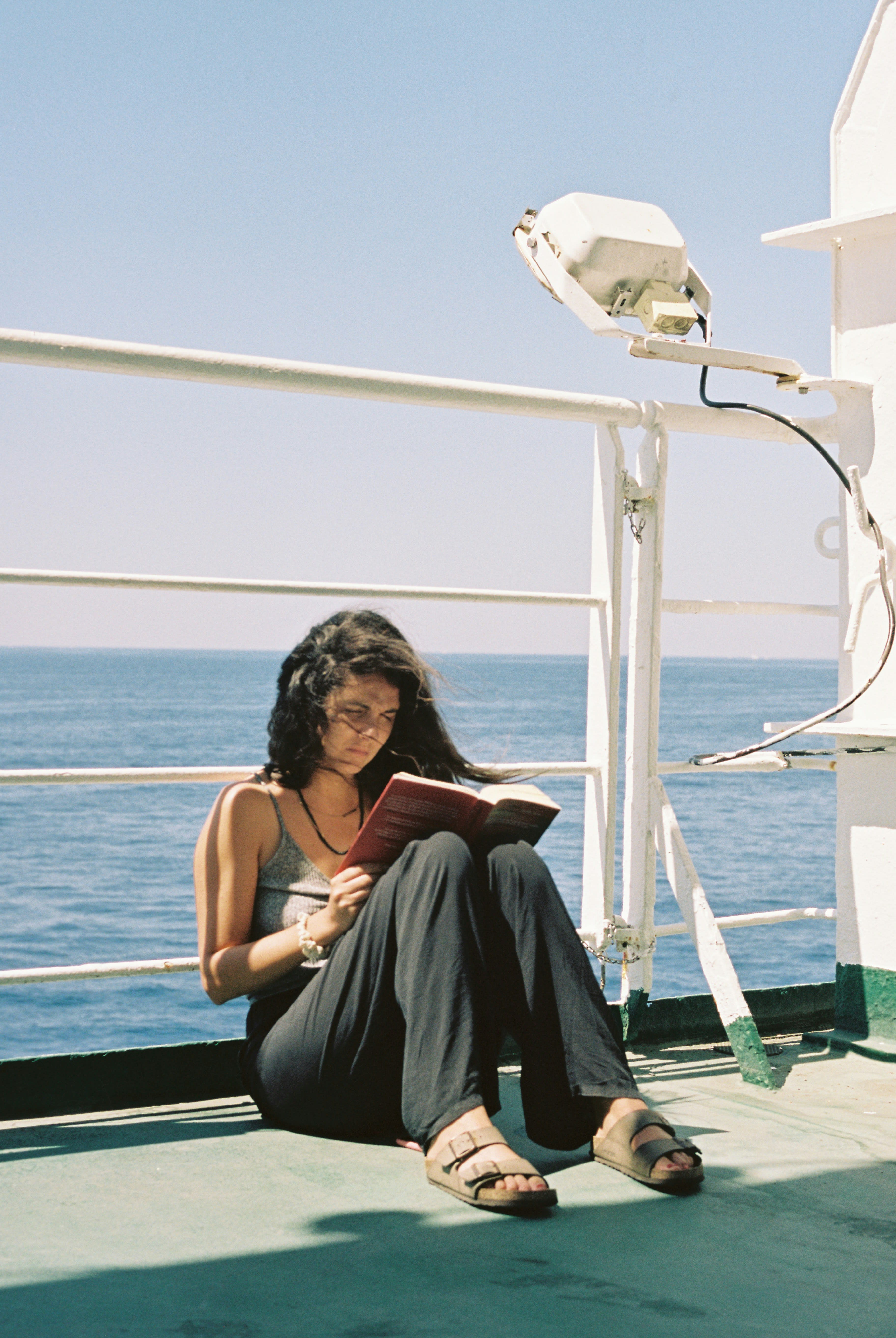 A woman reading a book on a ferry deck with the sea behind her
