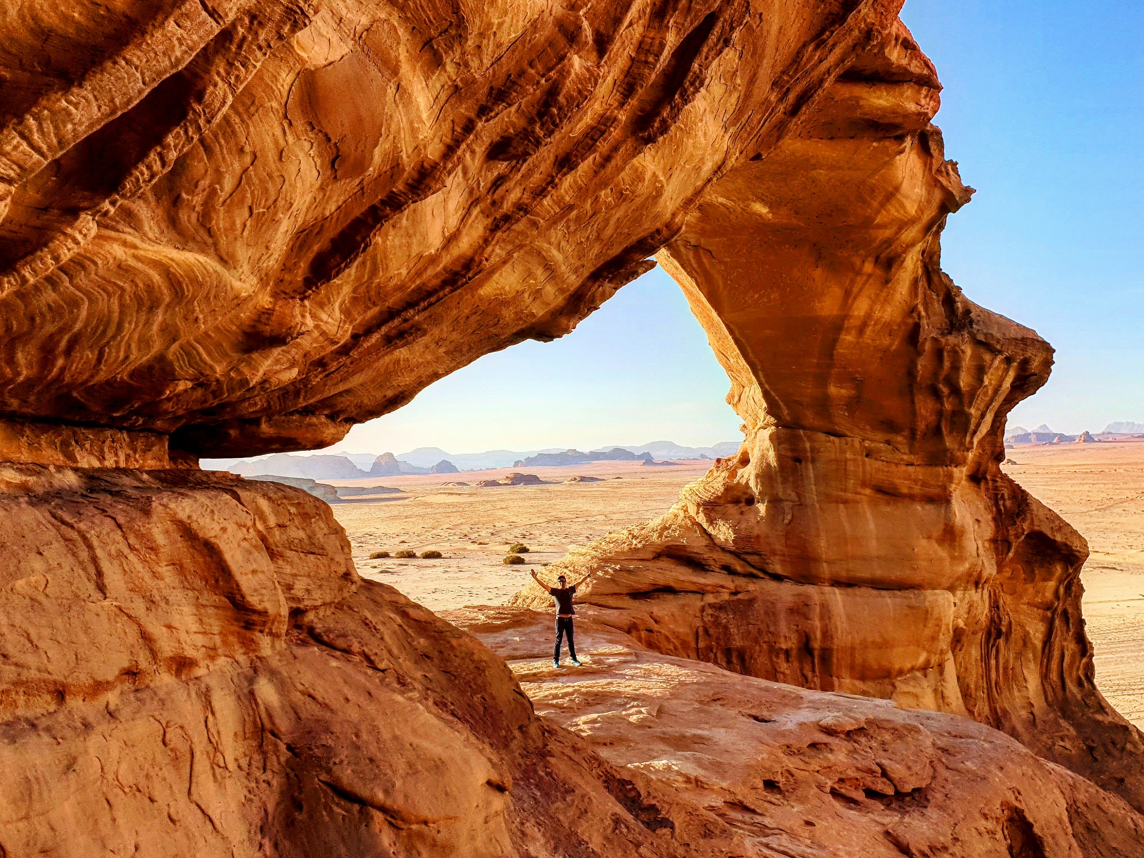 A natural sandstone arch high above the desert with a small figure standing beneath it