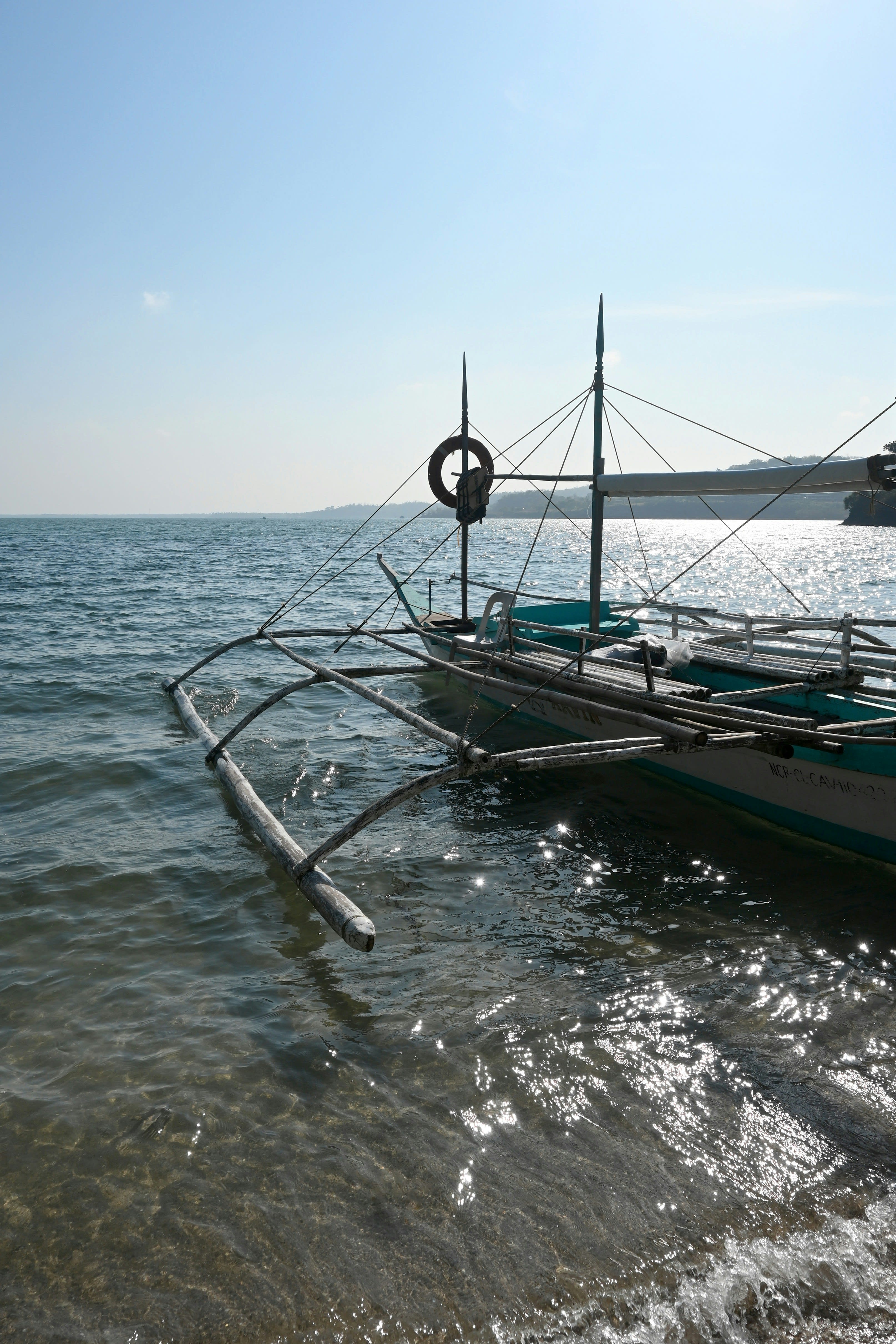 A white outrigger boat floating on clear shallow water