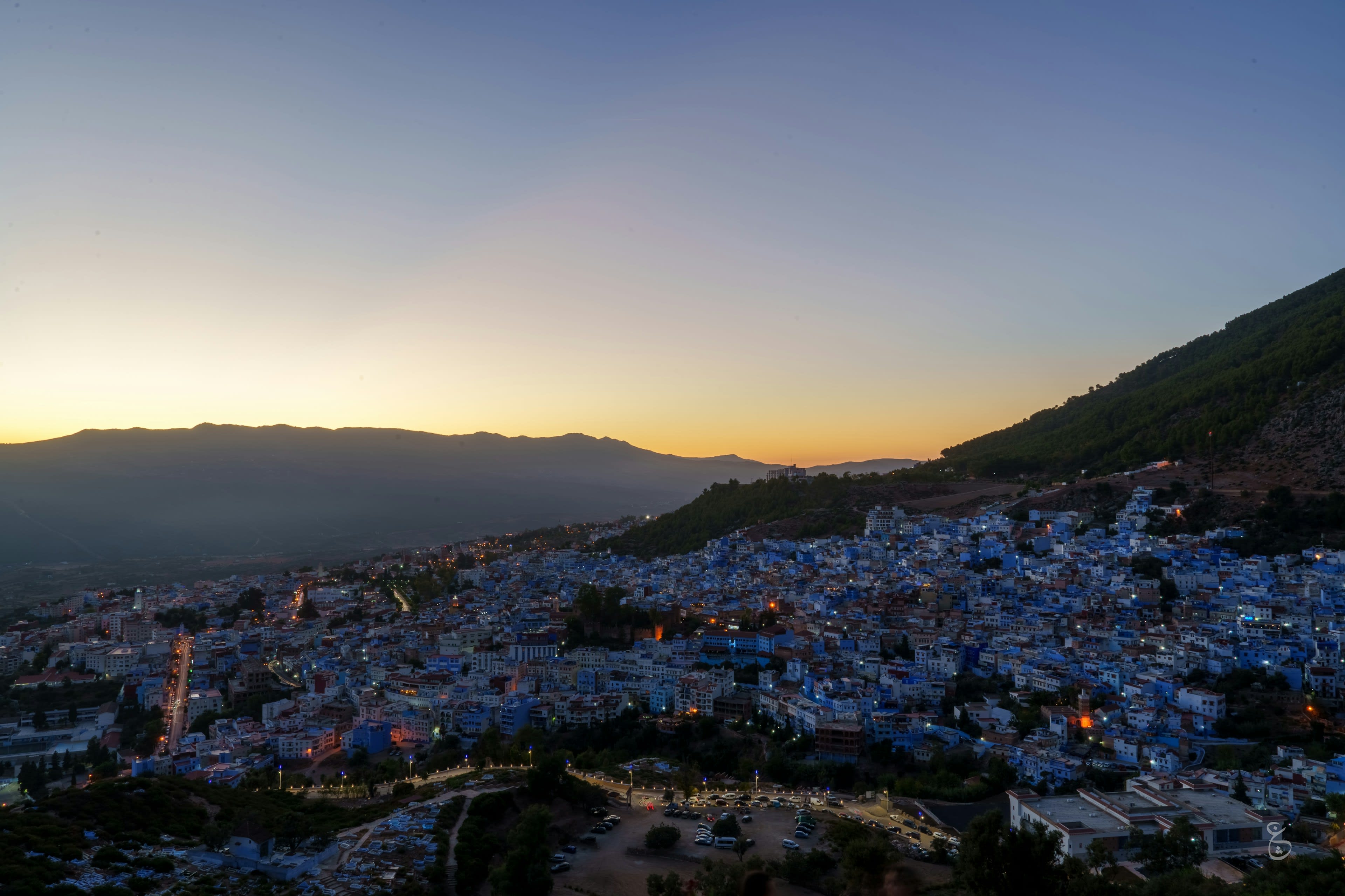 A blue town filling a valley below hazy mountains at first light