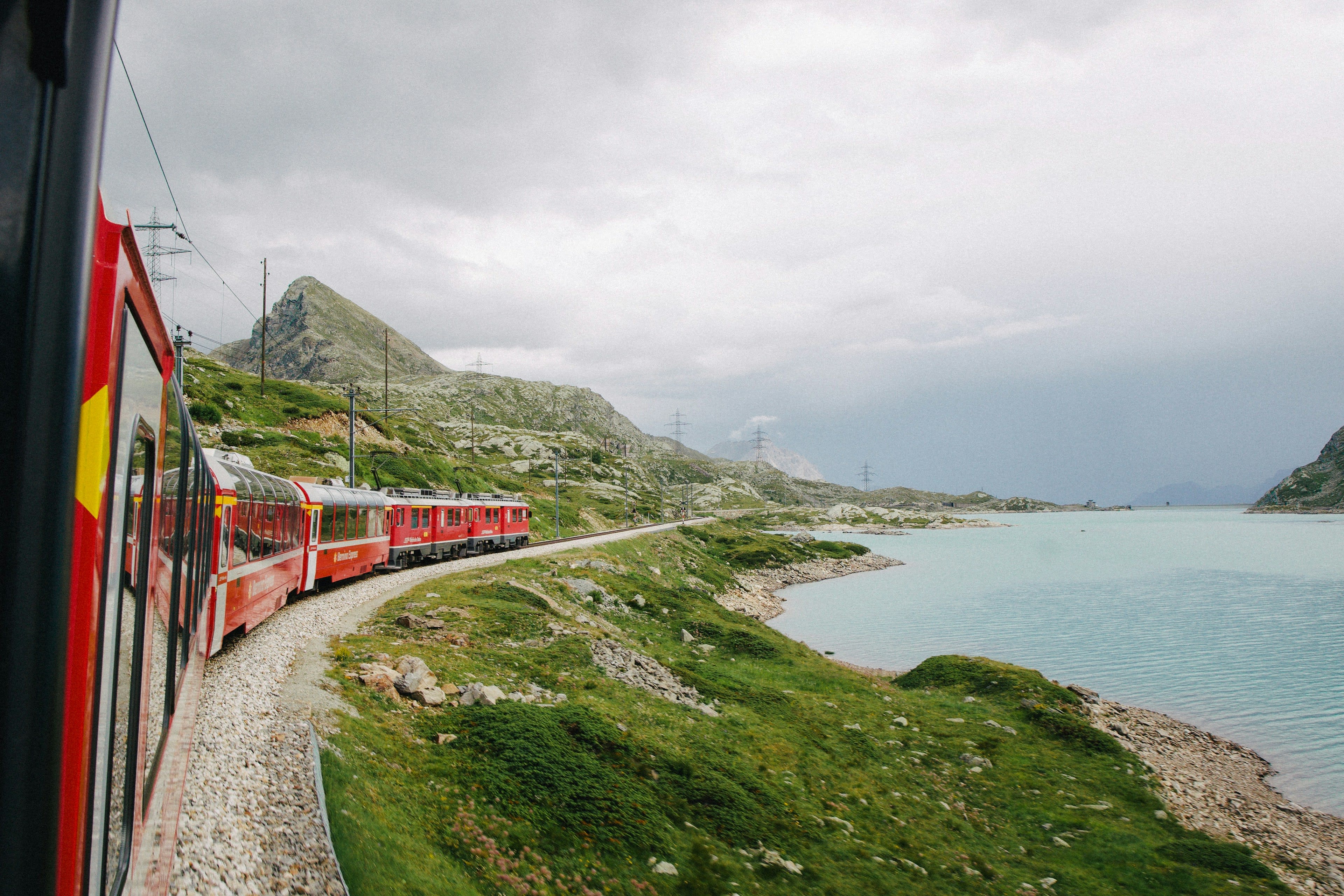View along a red train beside a pale mountain lake