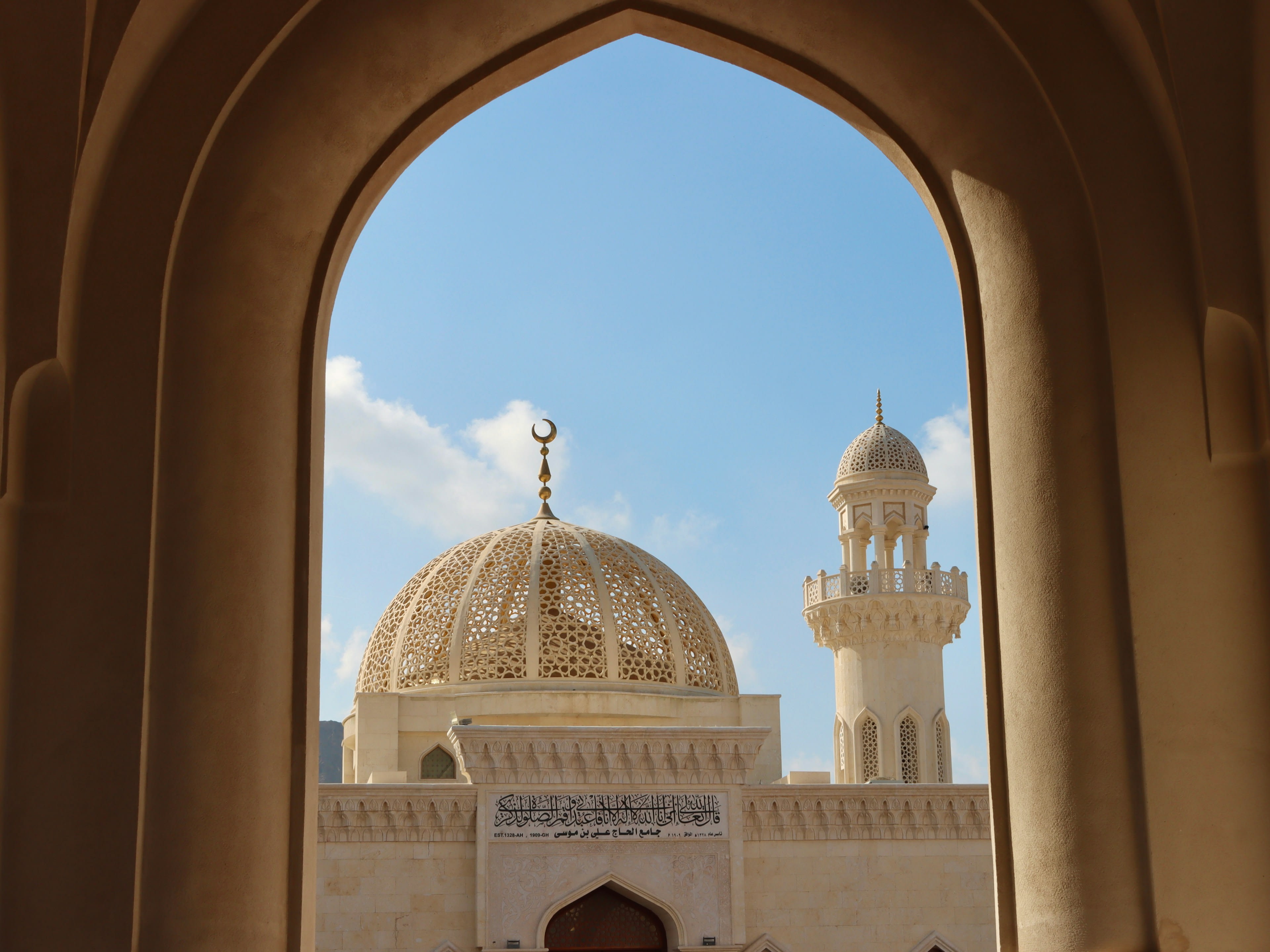 A white mosque with golden dome and tall minaret under blue sky