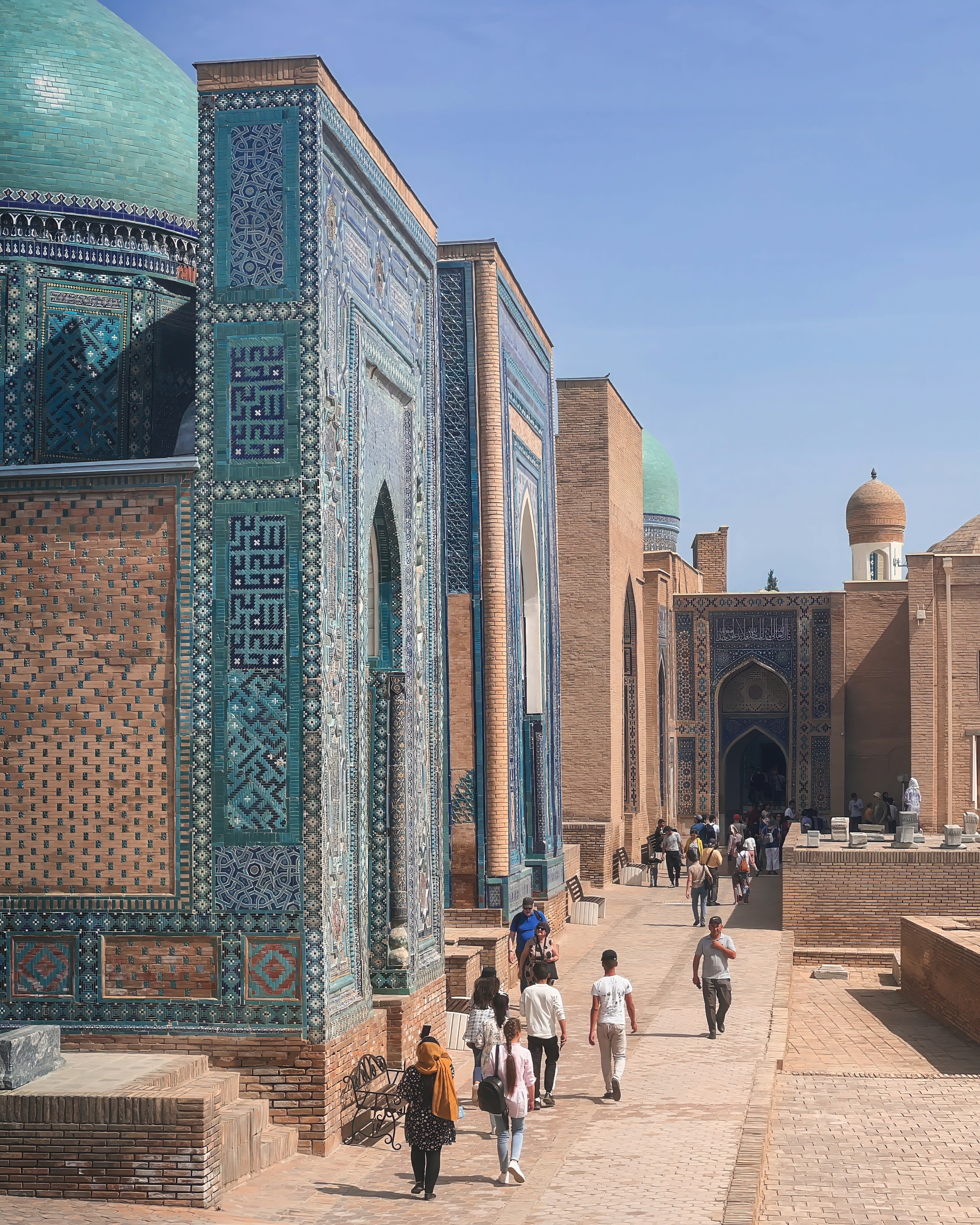 People walking a narrow lane between blue-tiled mausoleum facades