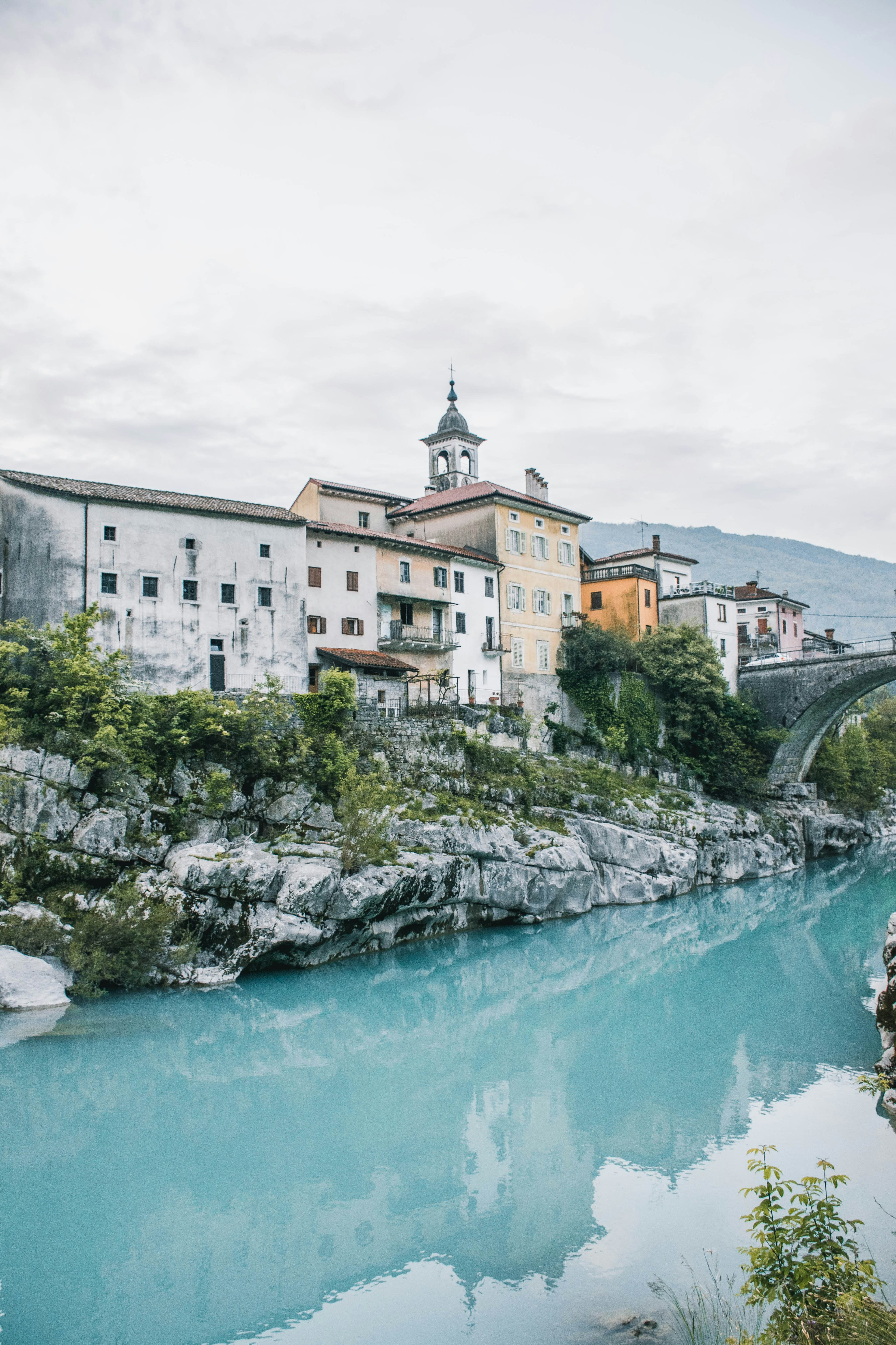 Old stone buildings above a milky turquoise alpine river