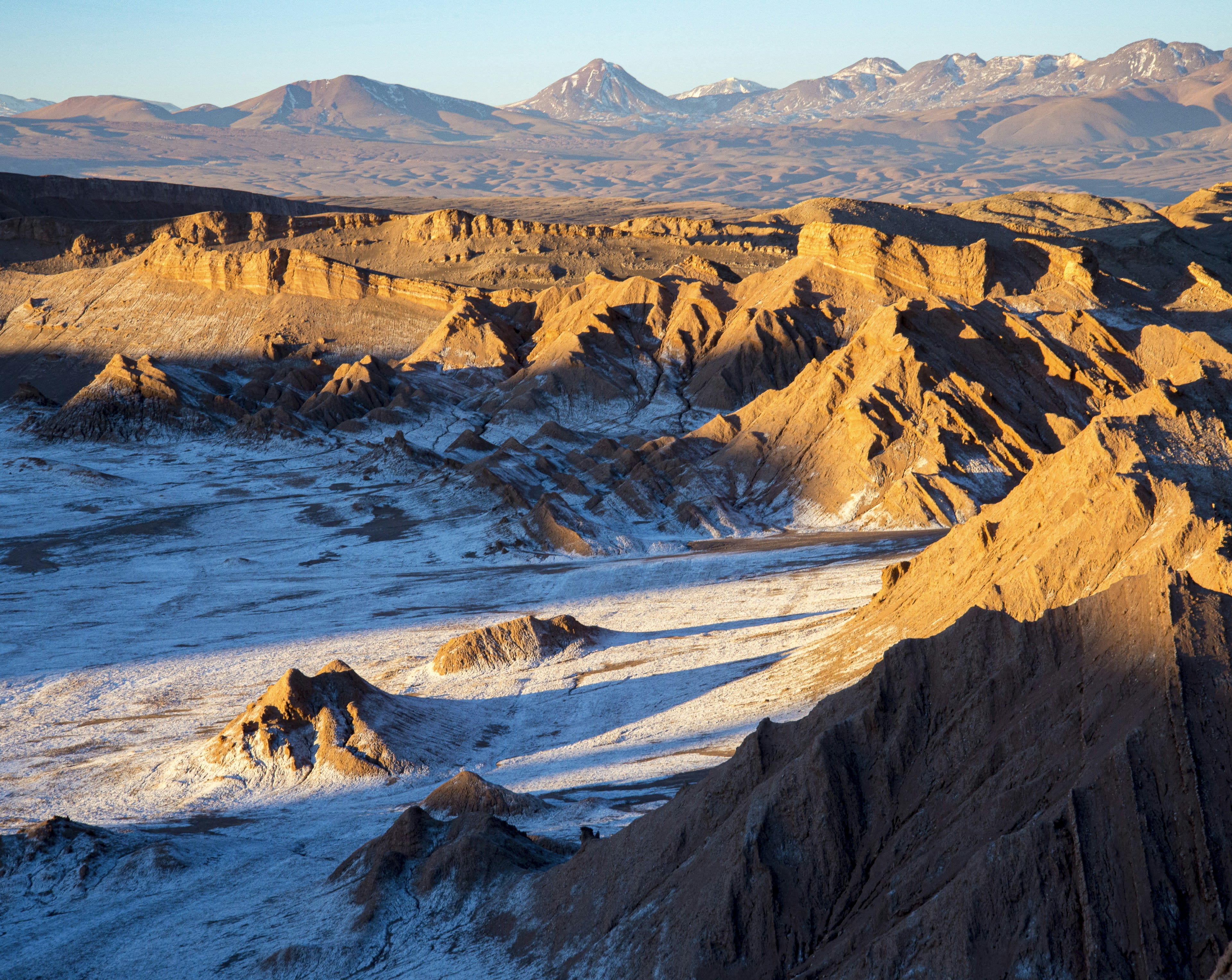 Salt-crusted ridges of the Valle de la Luna with distant volcanoes at golden hour