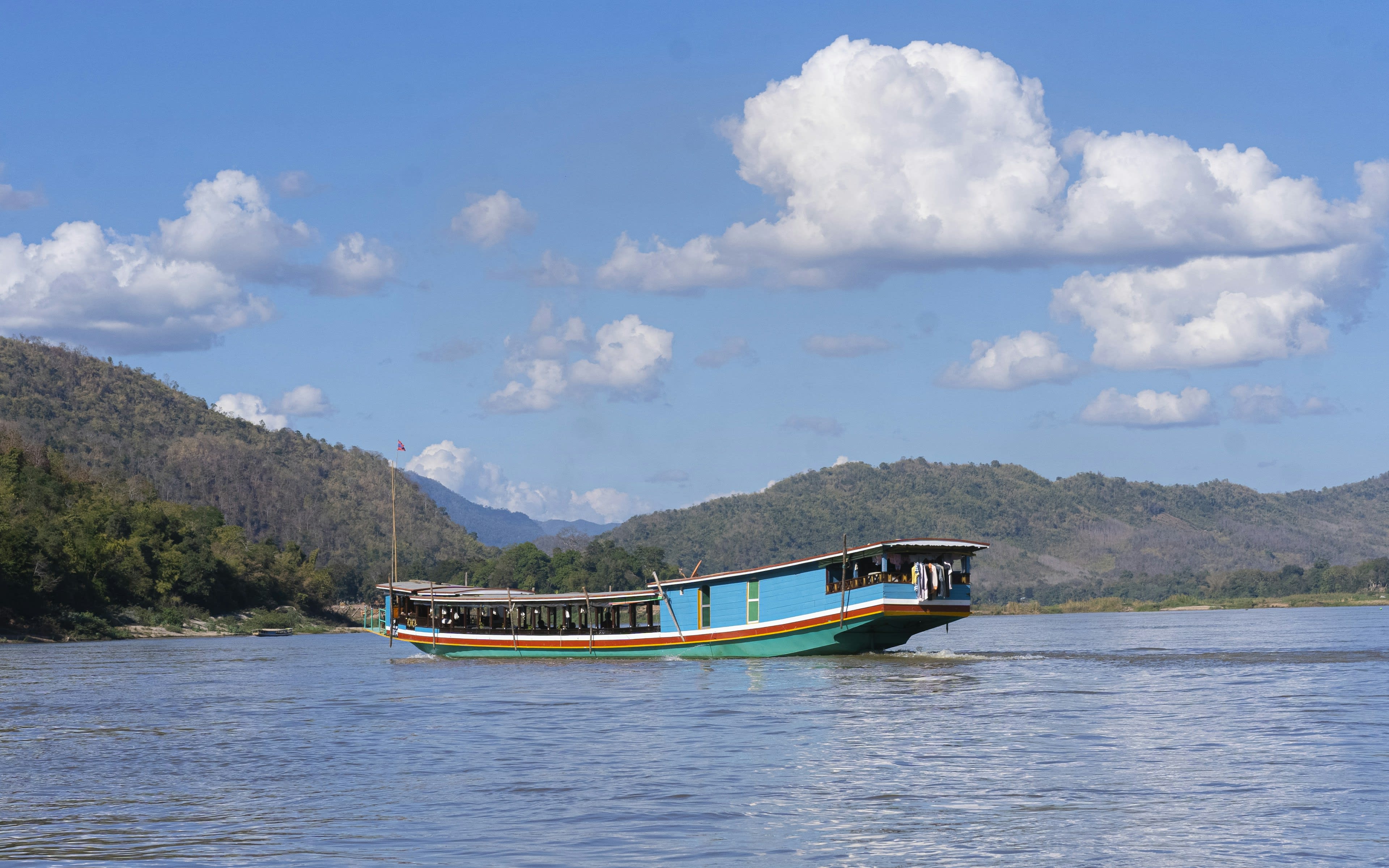A long wooden slow boat on the wide brown Mekong under hazy light