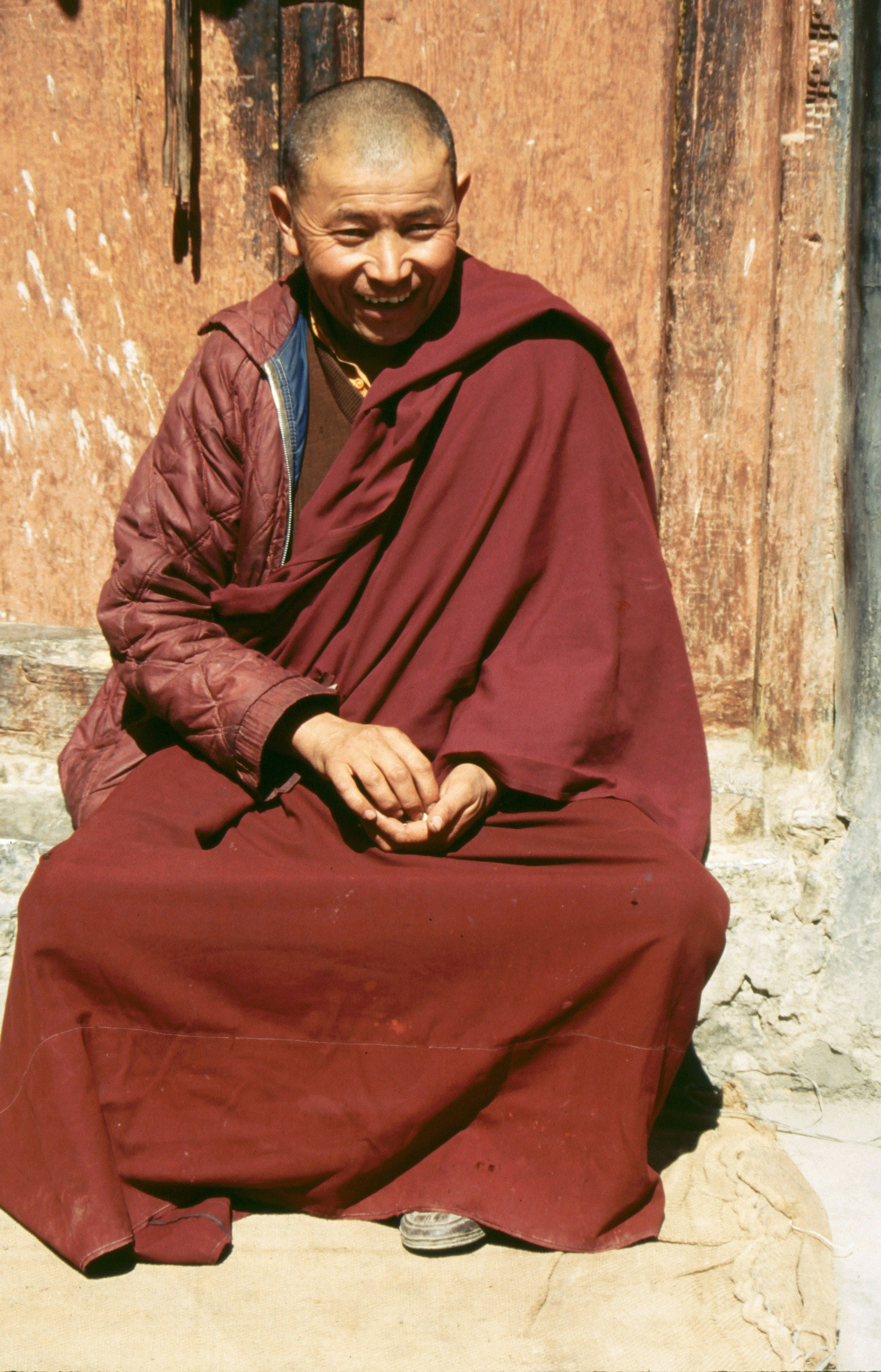 A young monk in maroon robes sitting and smiling at the camera