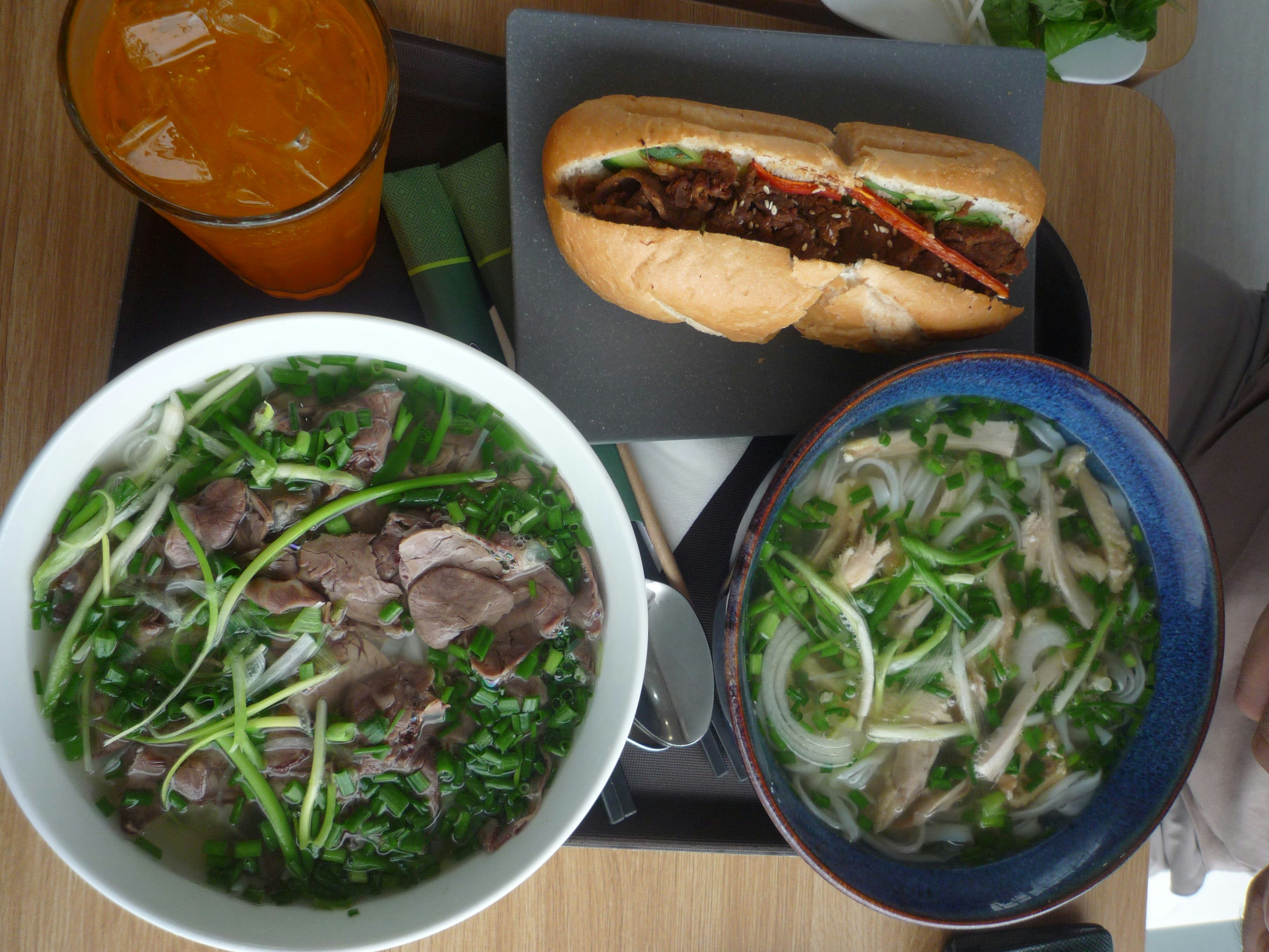Bowls of pho, a banh mi and juice on a breakfast table
