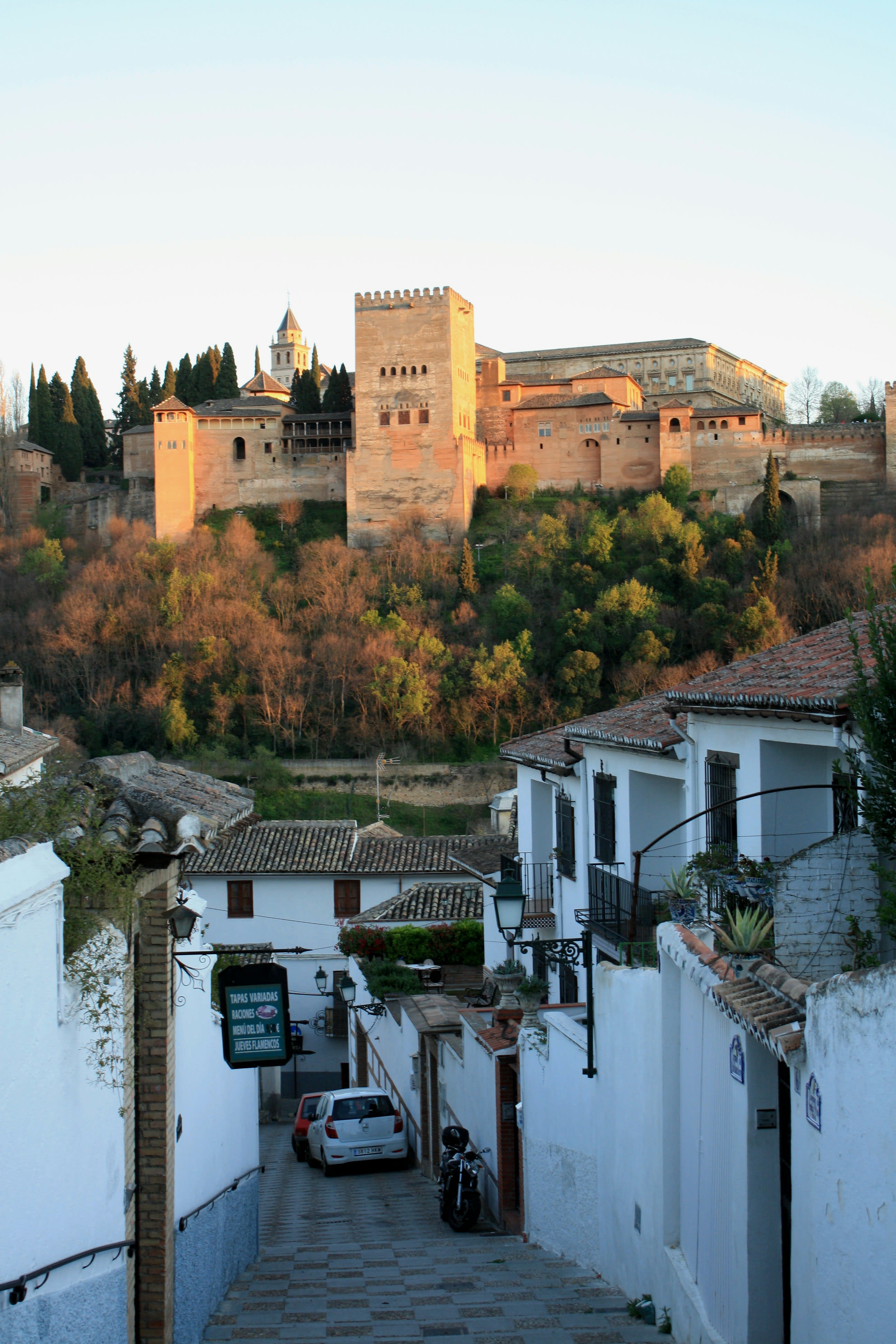 A whitewashed Granada lane framing the Alhambra on its hill in evening light