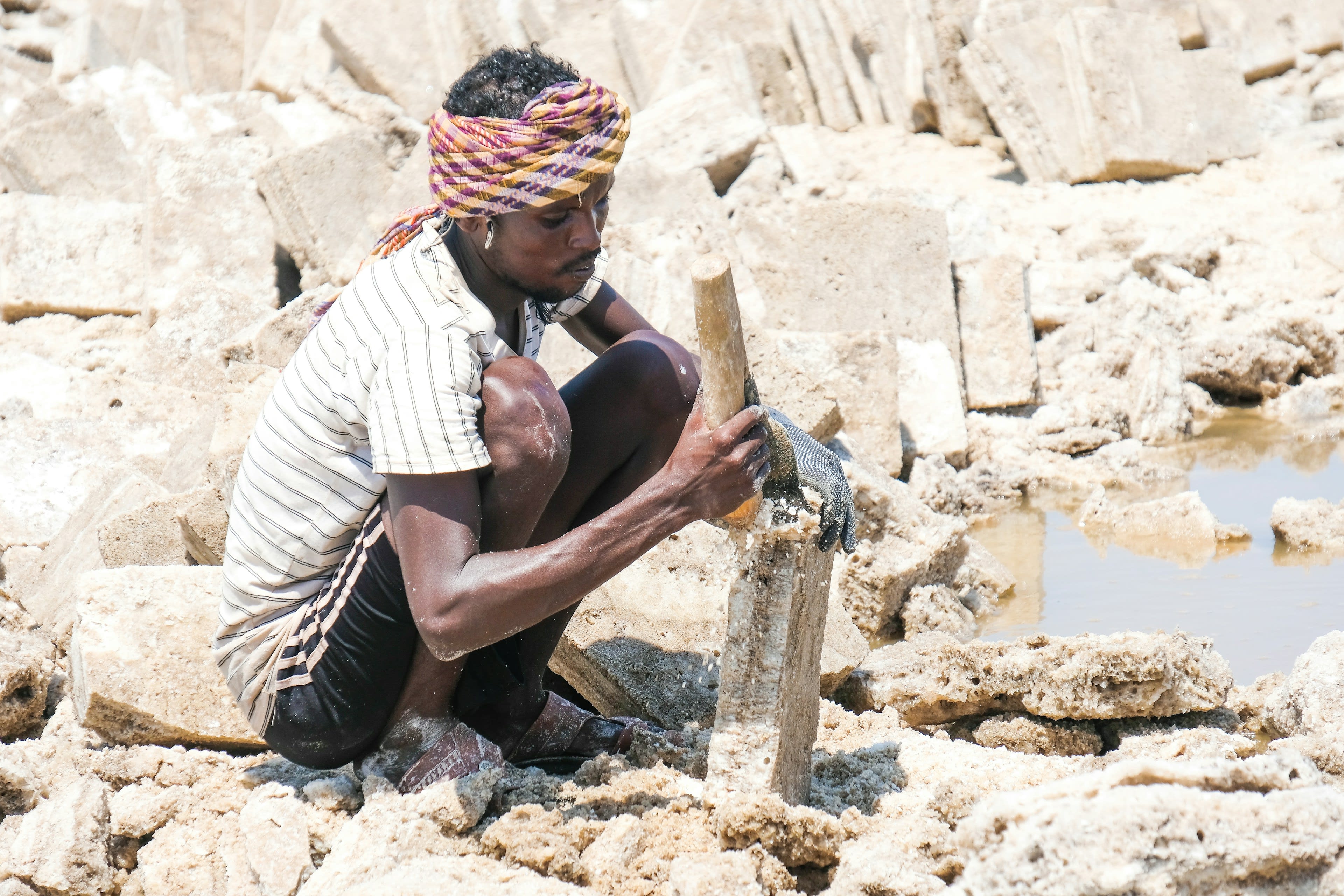 An Afar salt cutter in a red headscarf shaping salt blocks on the flats