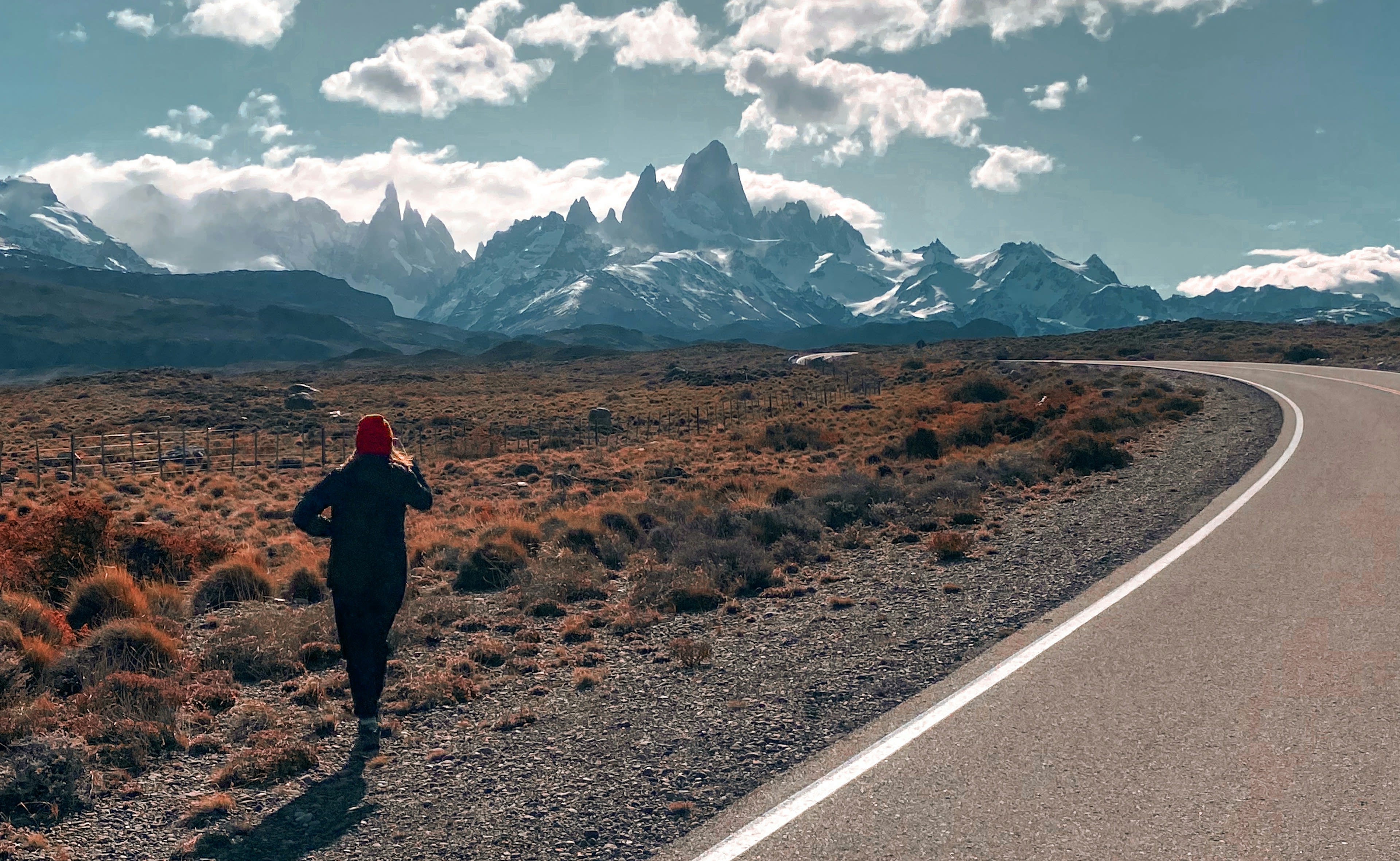 A person walking a paved road through orange scrub towards a distant granite range