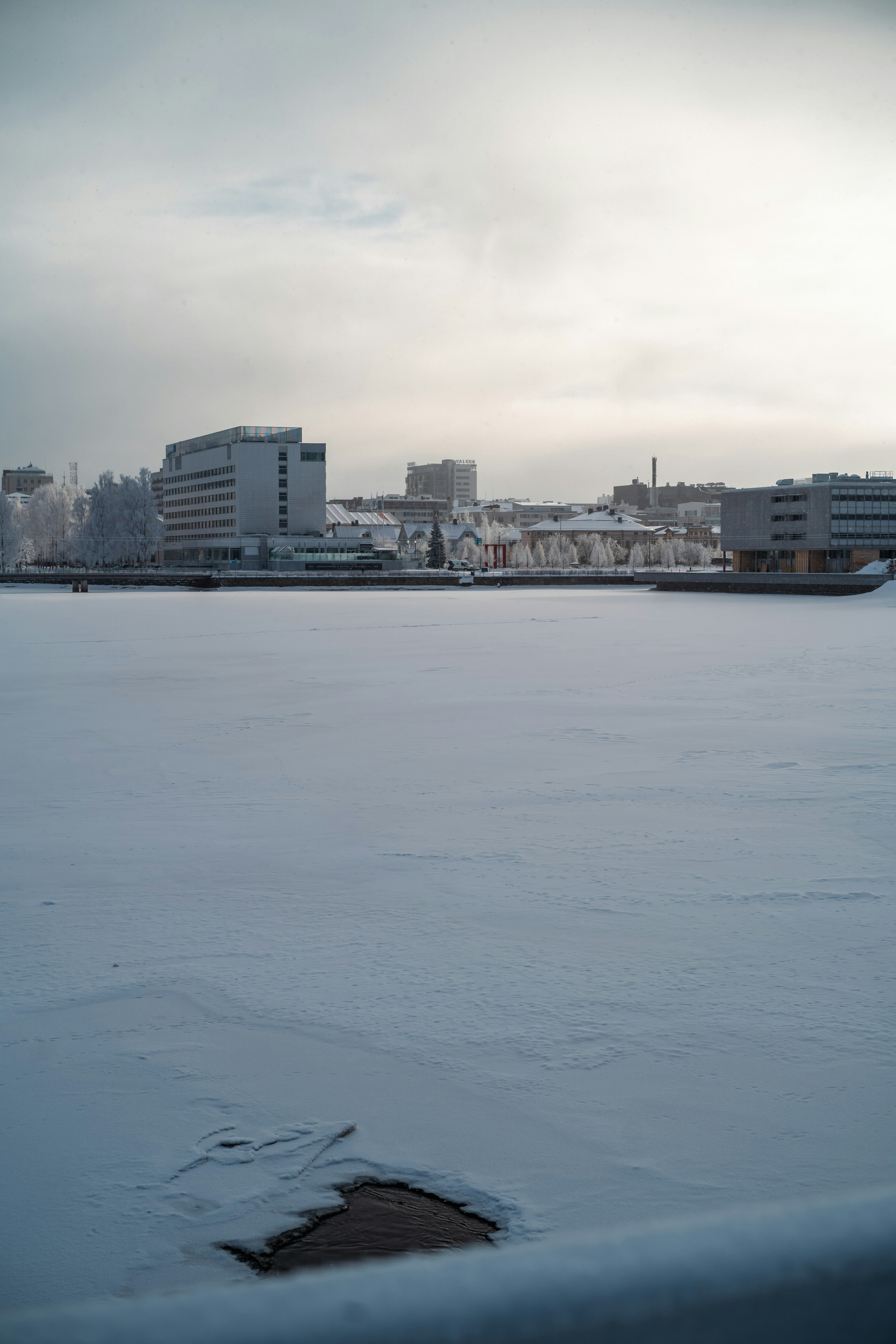 A frozen river in the foreground with low city buildings beyond