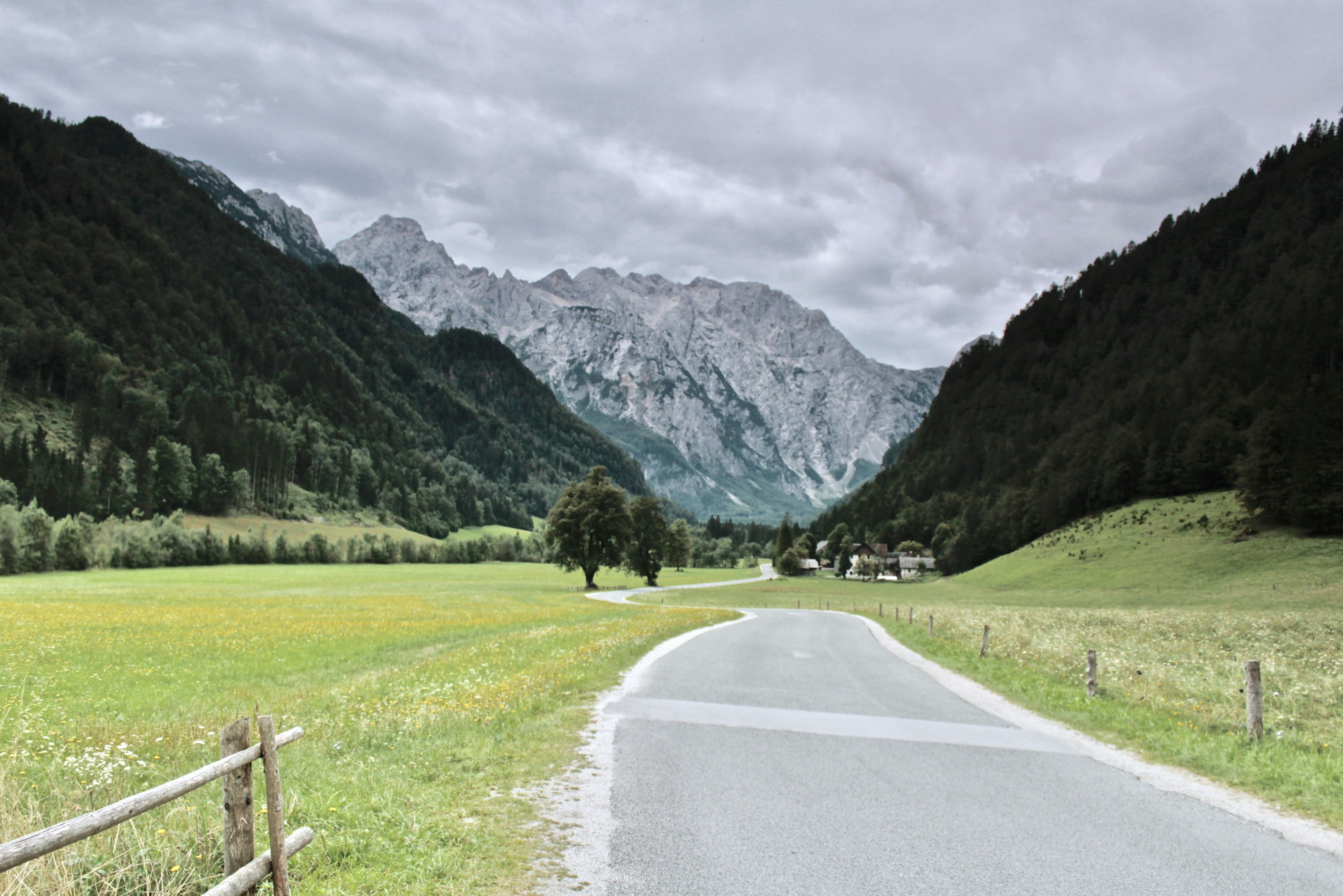 A road descending through green alpine meadows toward high peaks