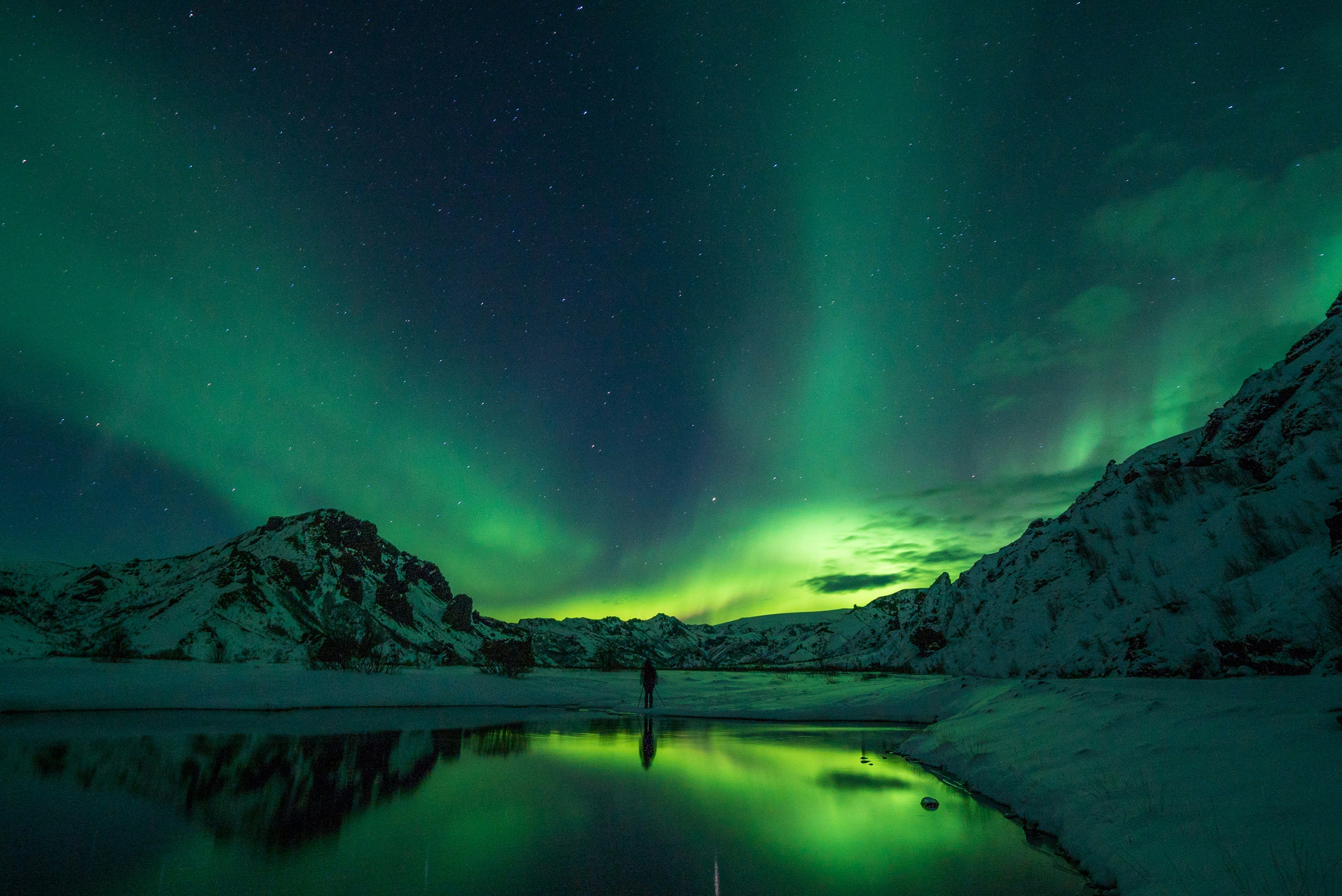 Green aurora over a dark mountain reflected in still water at night
