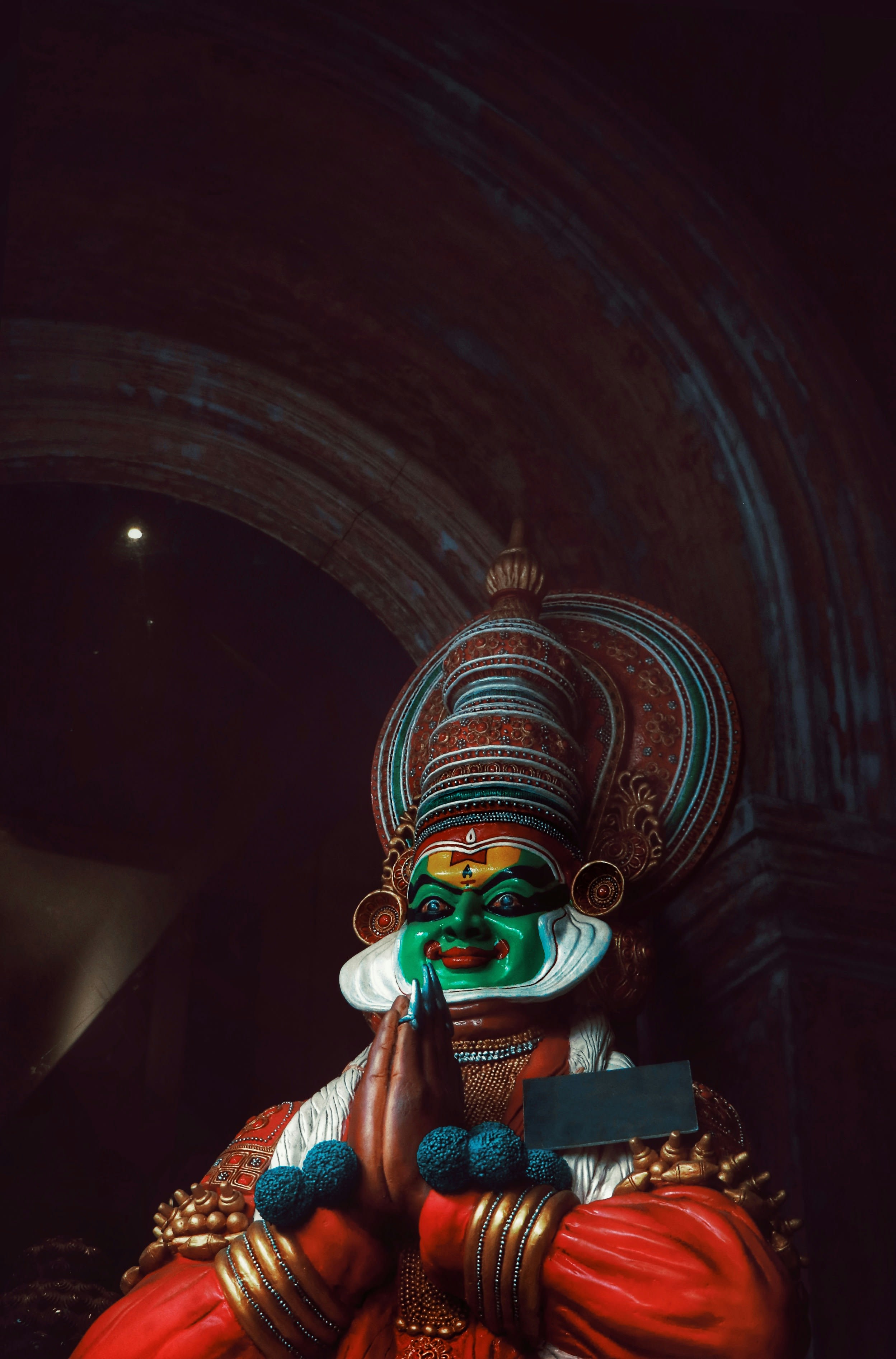 A Kathakali performer in elaborate green and red makeup and headdress under low light
