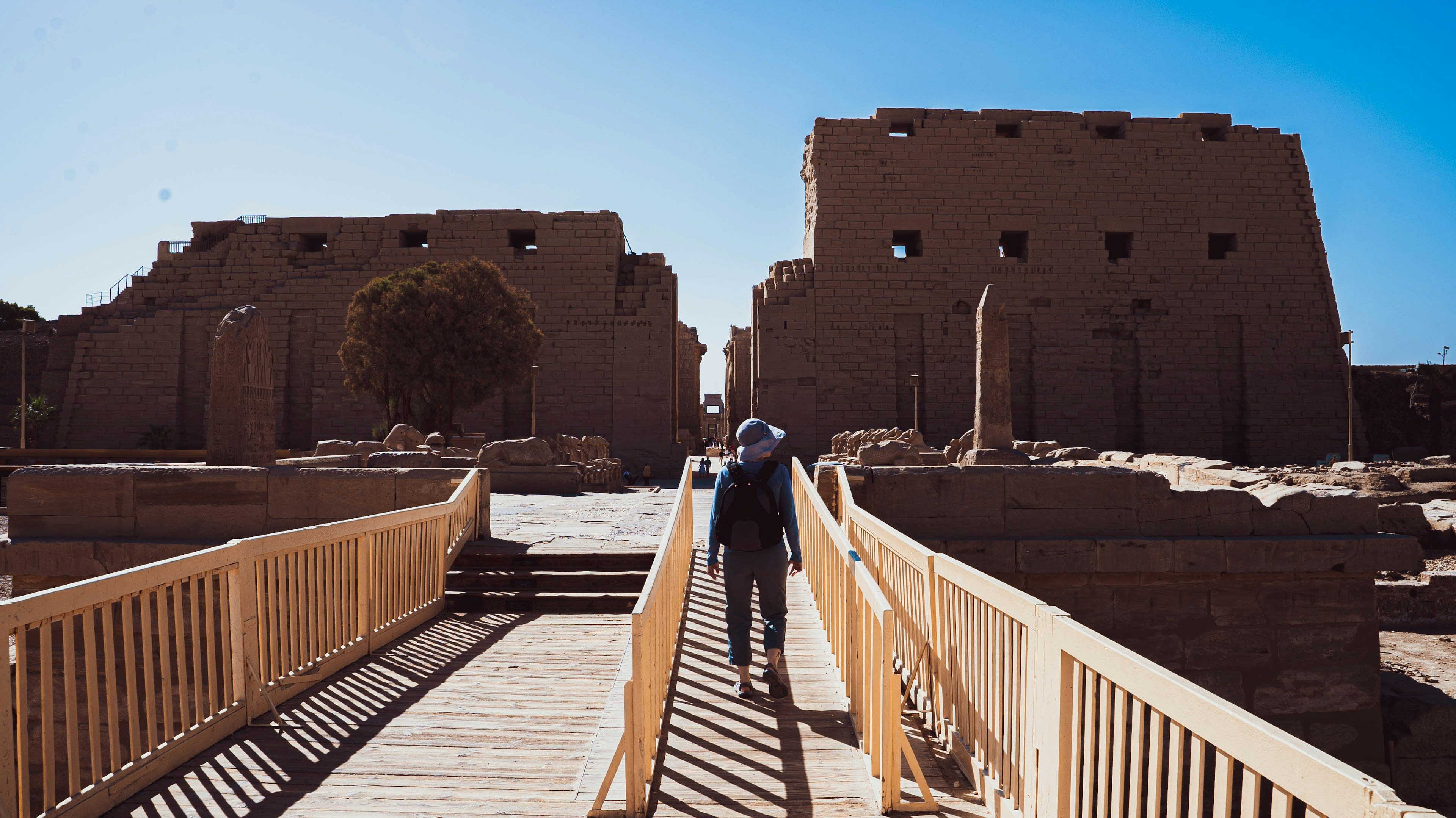 A lone figure walking a raised walkway through the ruins of Karnak