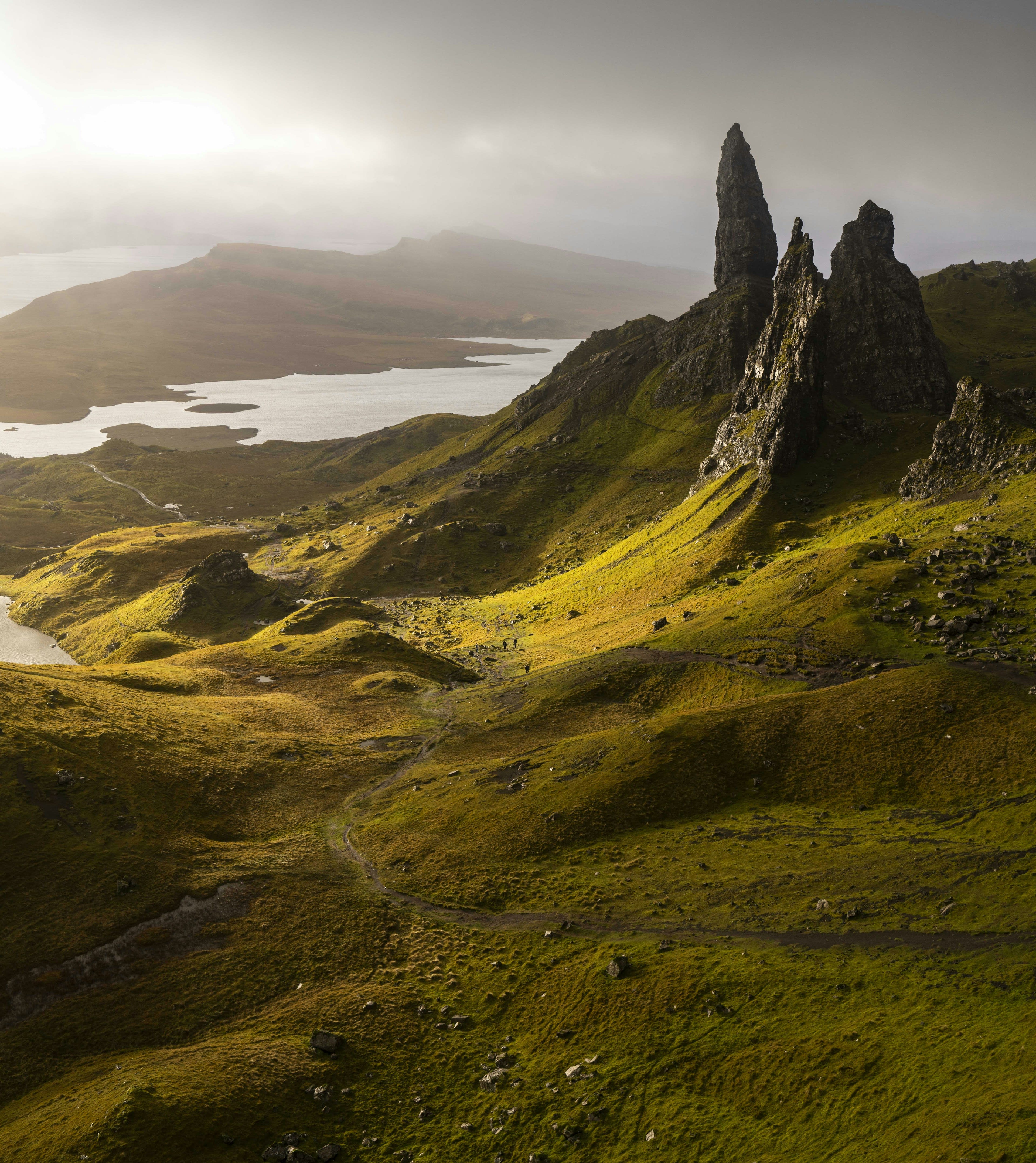 The same rock pinnacles lit gold by low sun above a hazy sea loch