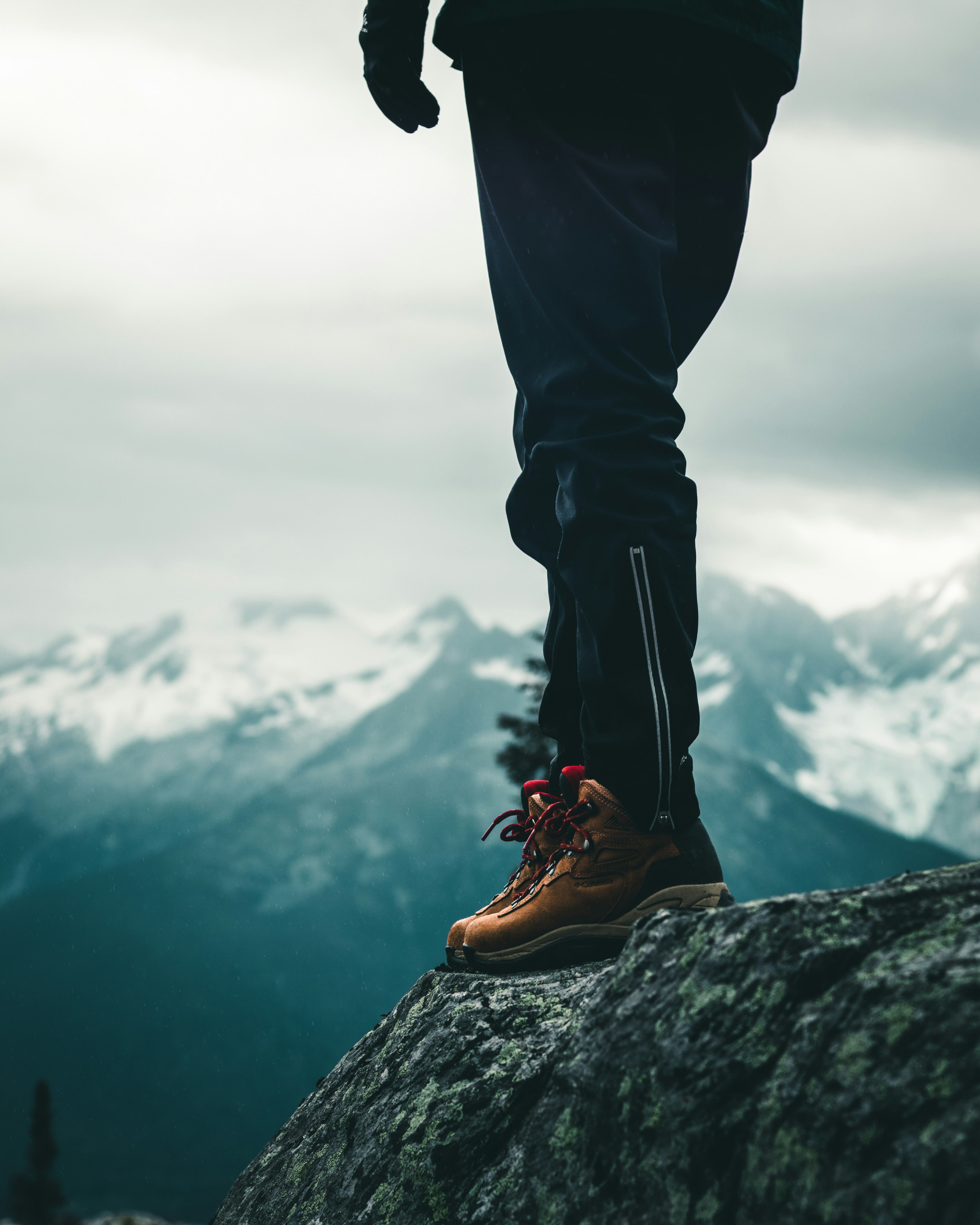 Worn leather boots and legs standing on rock above a cloud-filled valley