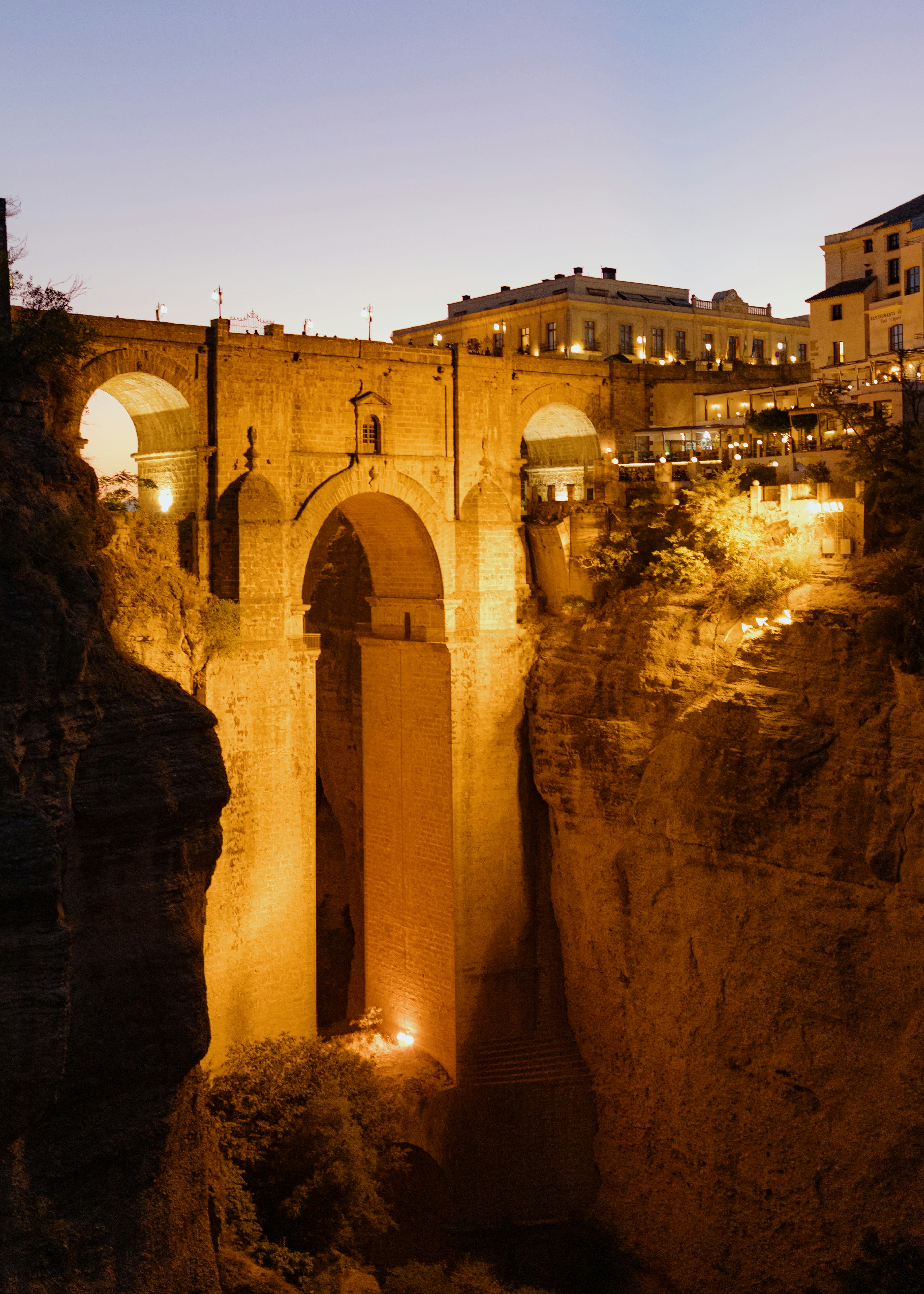 The tall stone bridge of Ronda spanning a gorge, floodlit at dusk