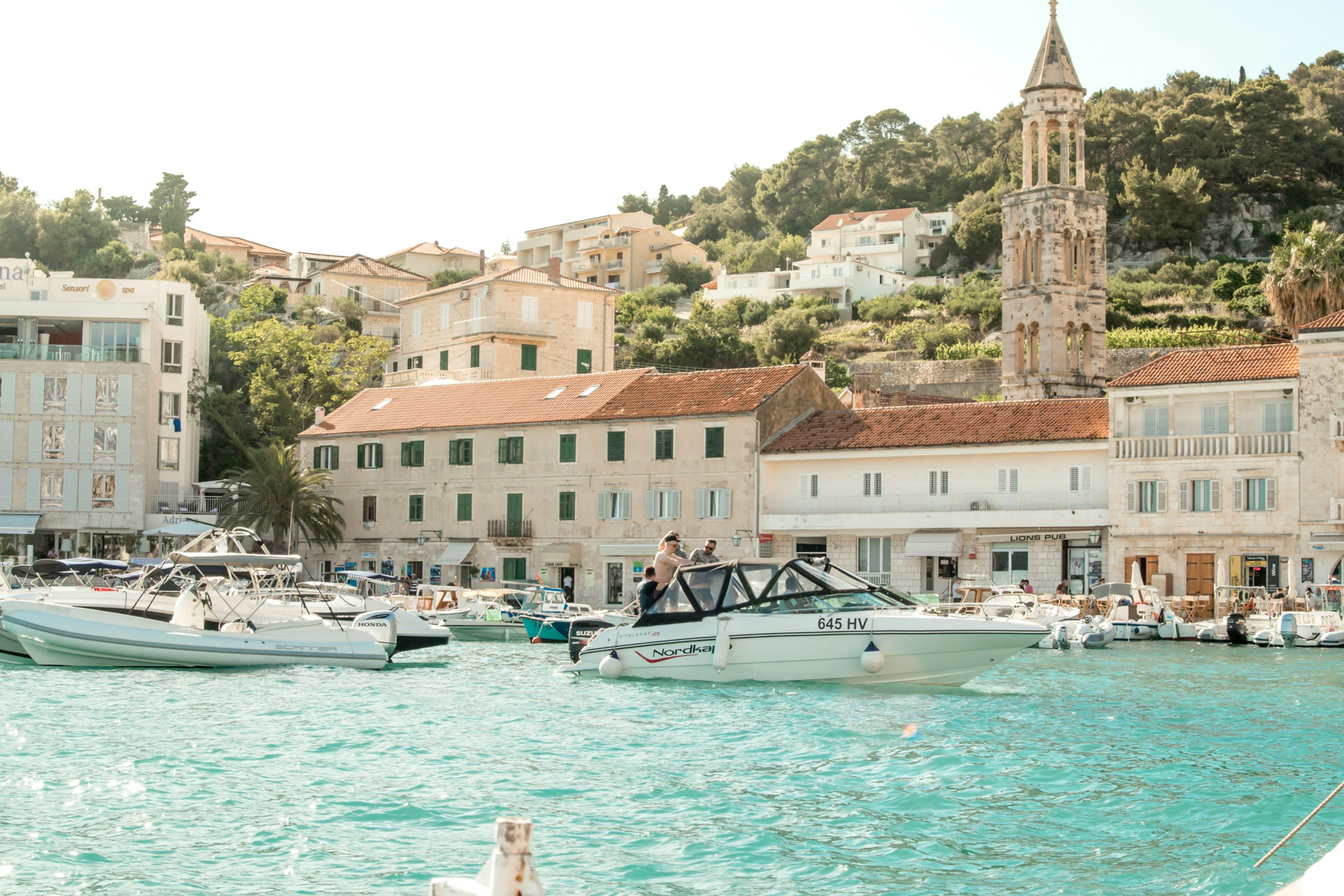 White boats moored in Hvar harbour seen from above, red roofs along the shore
