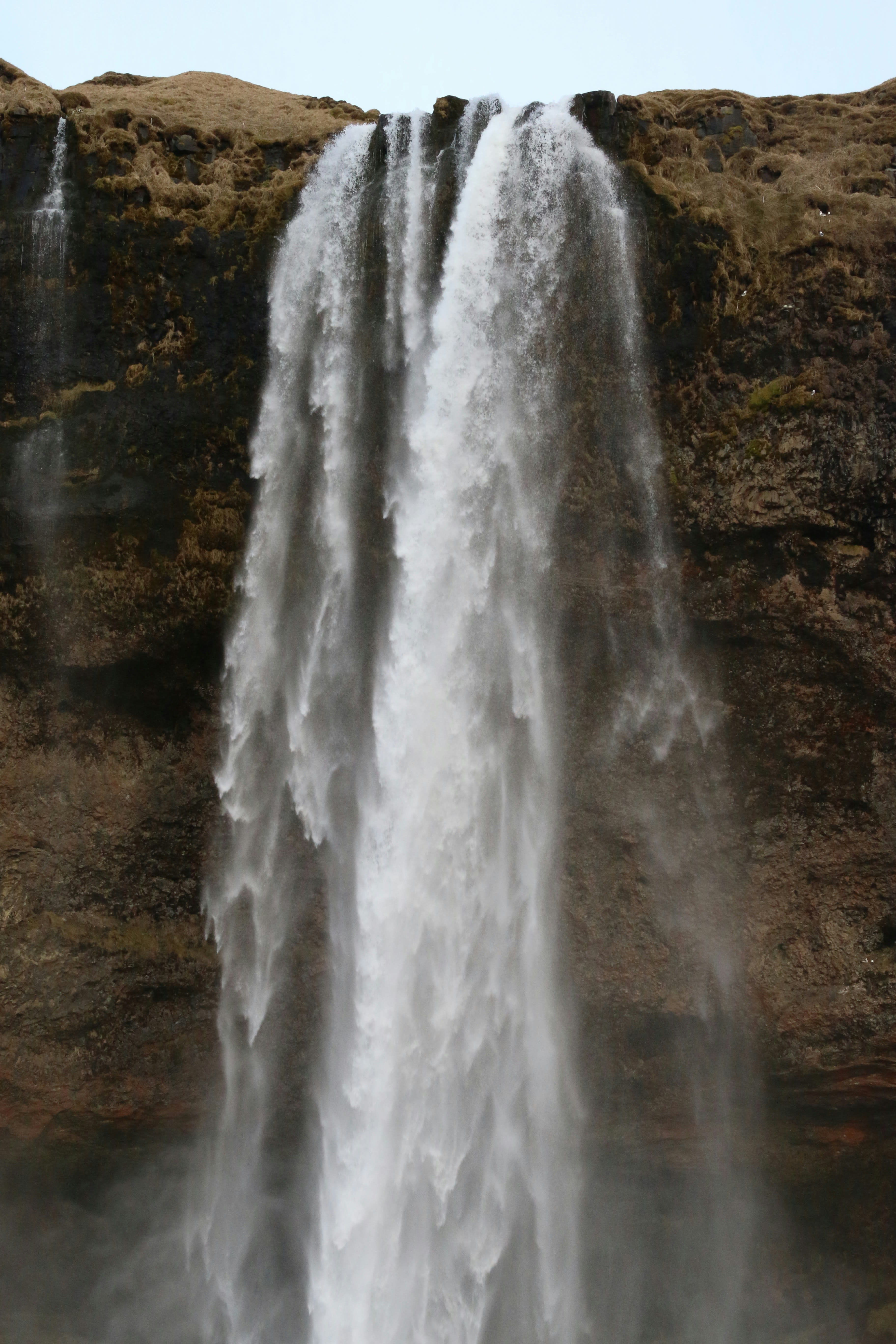 A wide waterfall falling over a dark cliff into a boulder field