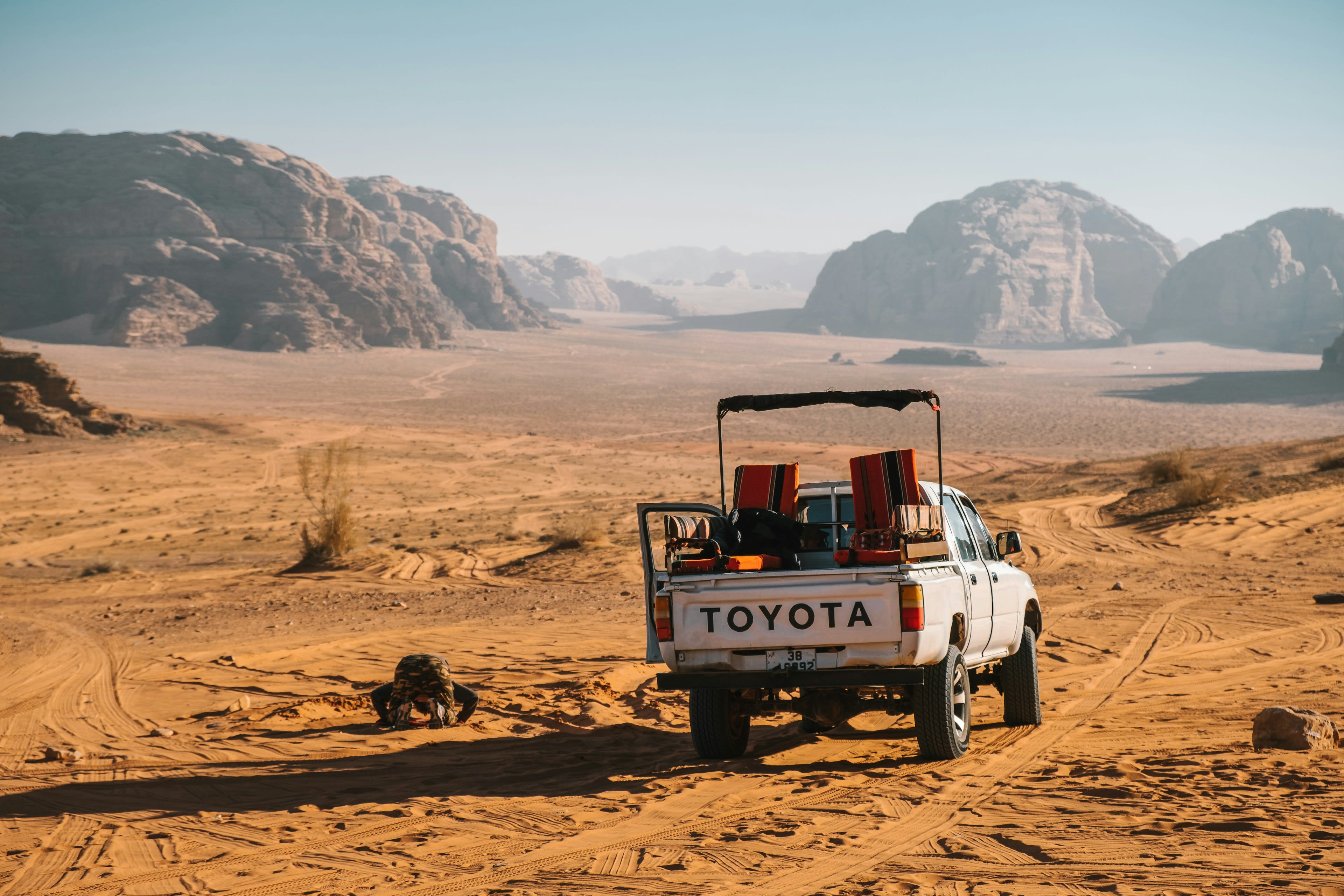 A white pickup truck with bench seating parked on red desert sand