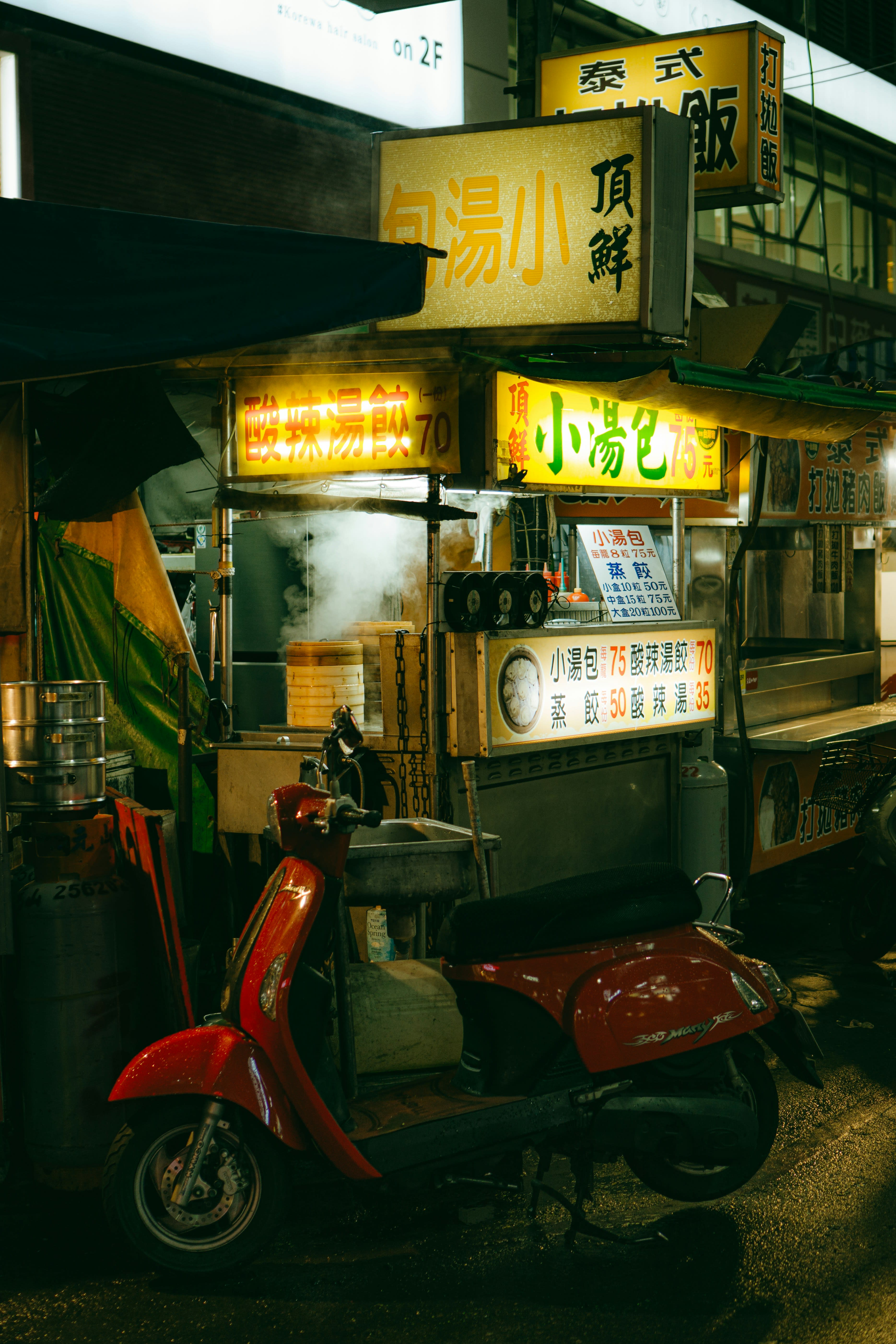 A red scooter parked in front of a brightly lit street food stall at night