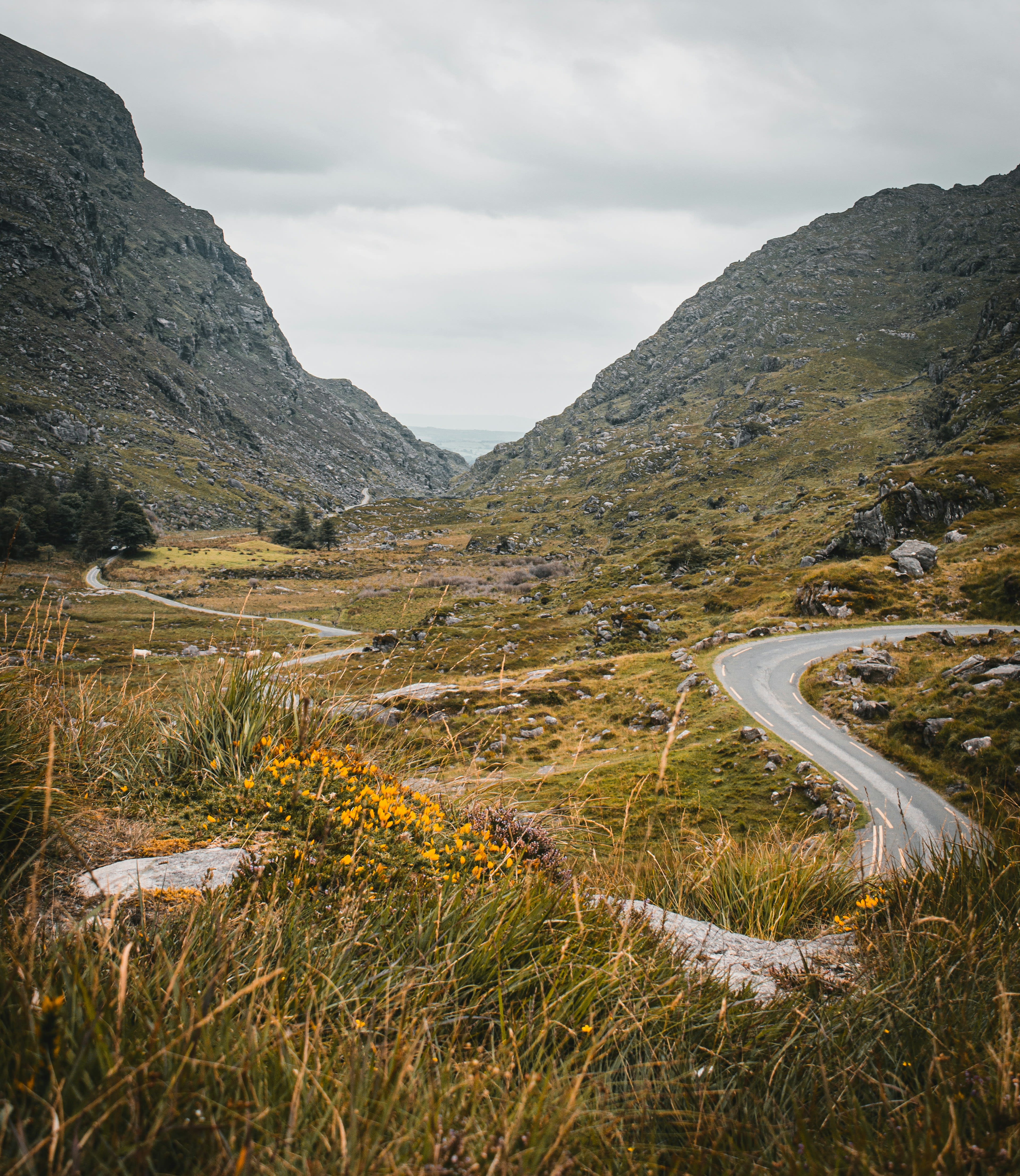 A narrow road winding through a rocky mountain pass with a dark lake below