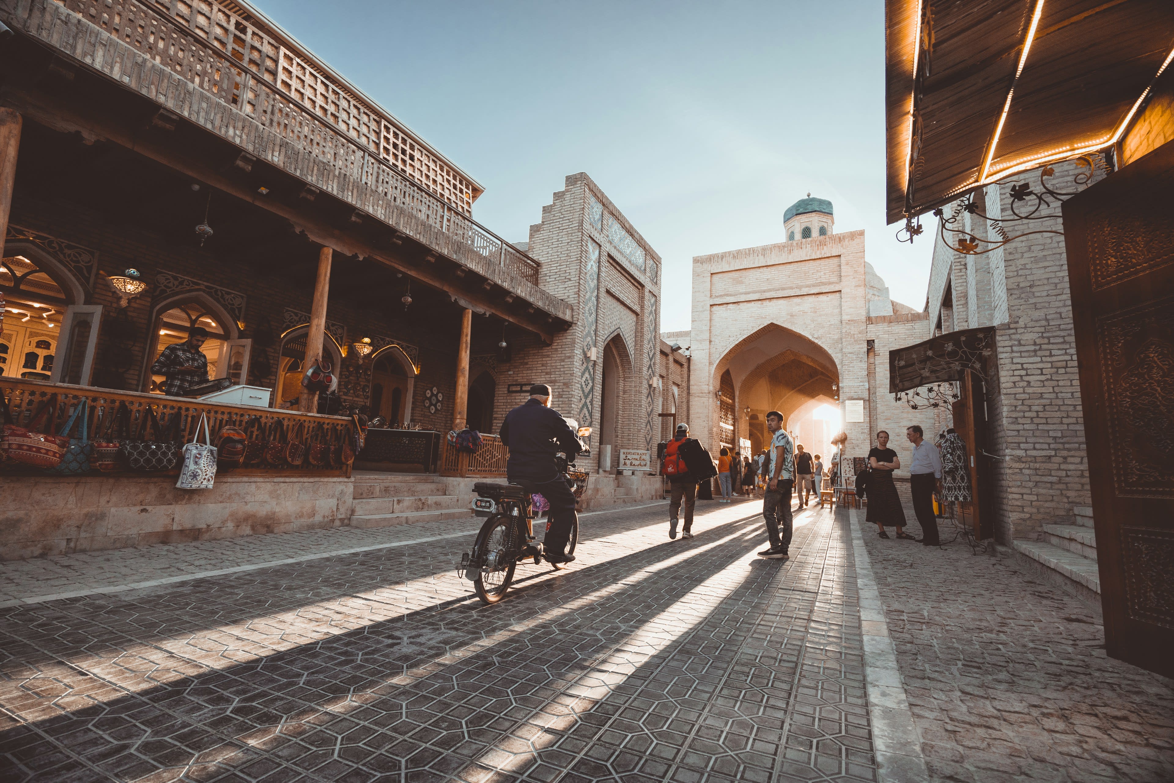 A cyclist riding a brick street between domed bazaar buildings in low sun