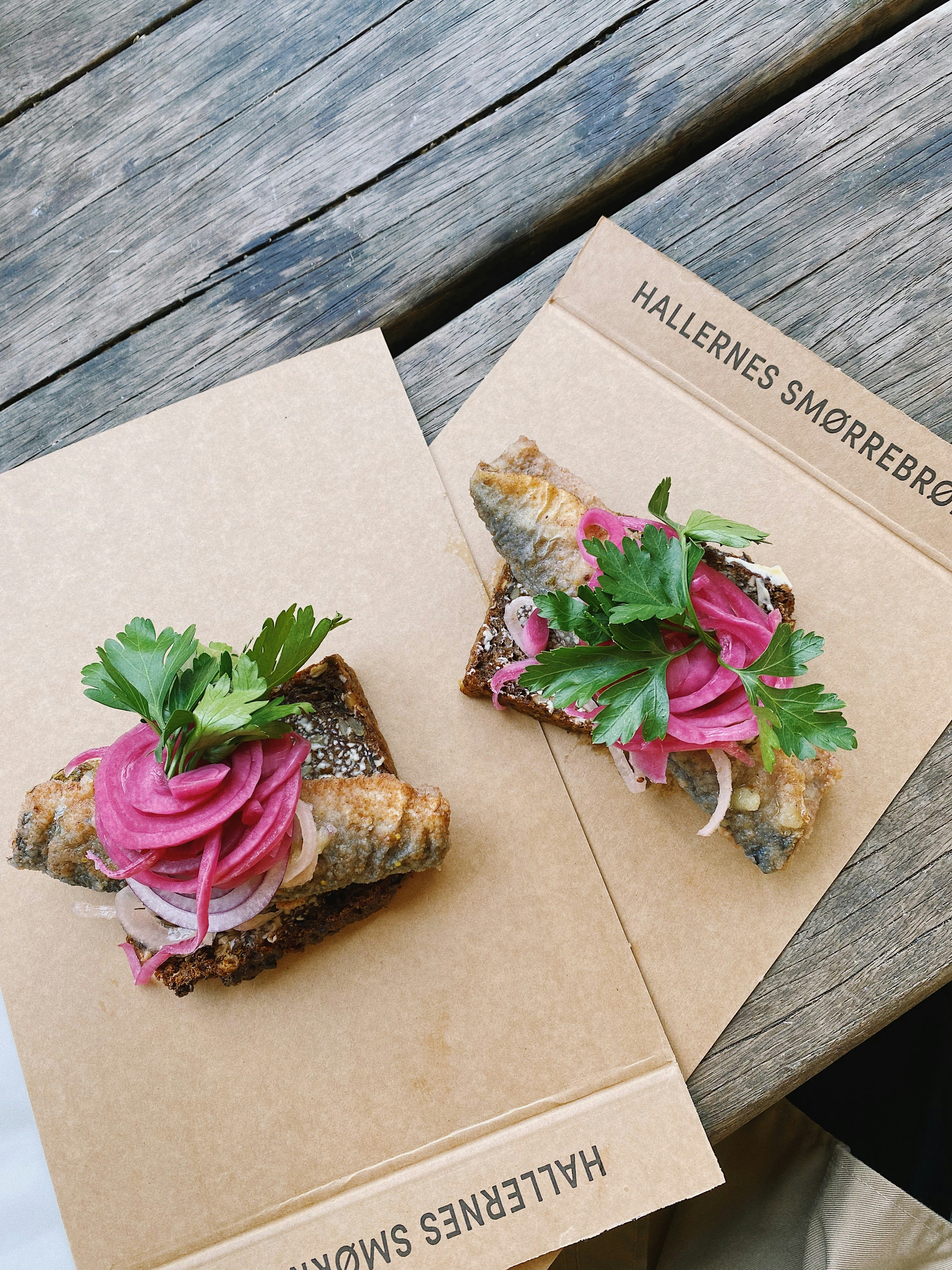 Two open-faced smørrebrød sandwiches on brown paper